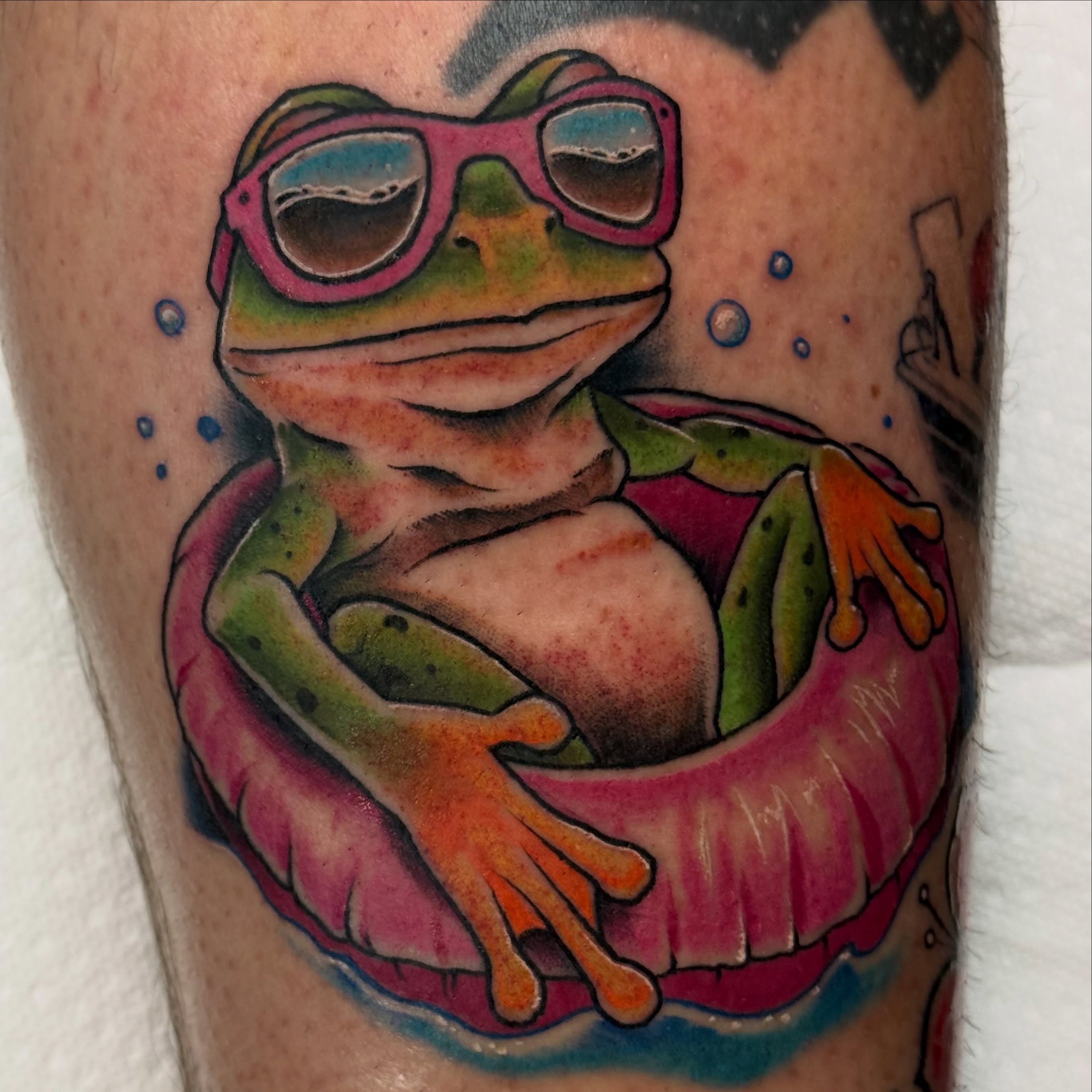 Frog in float new school tattoo on the upper arm by Justin Hay