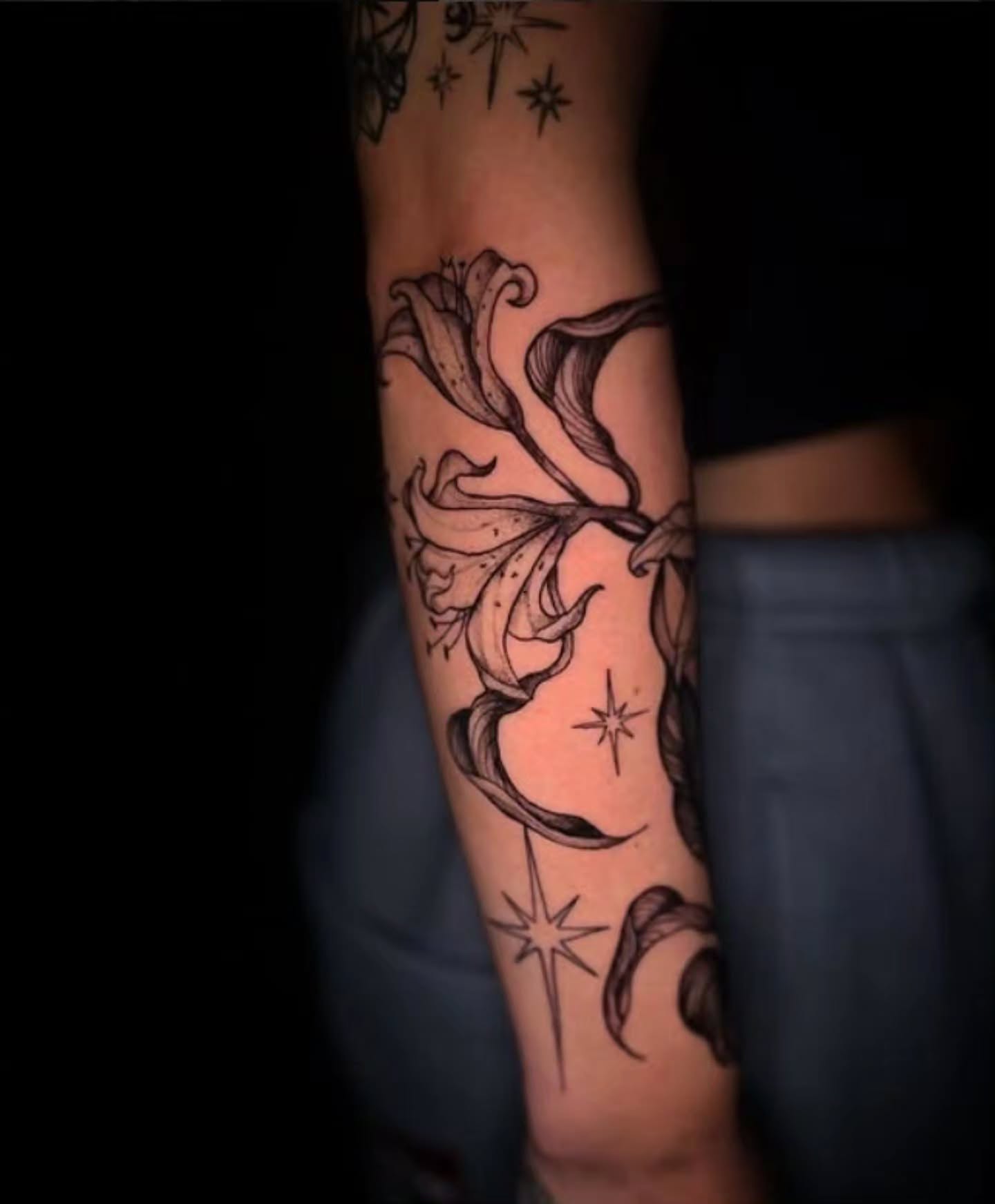 Lily and stars black and grey tattoo on the forearm by Angie Milano
