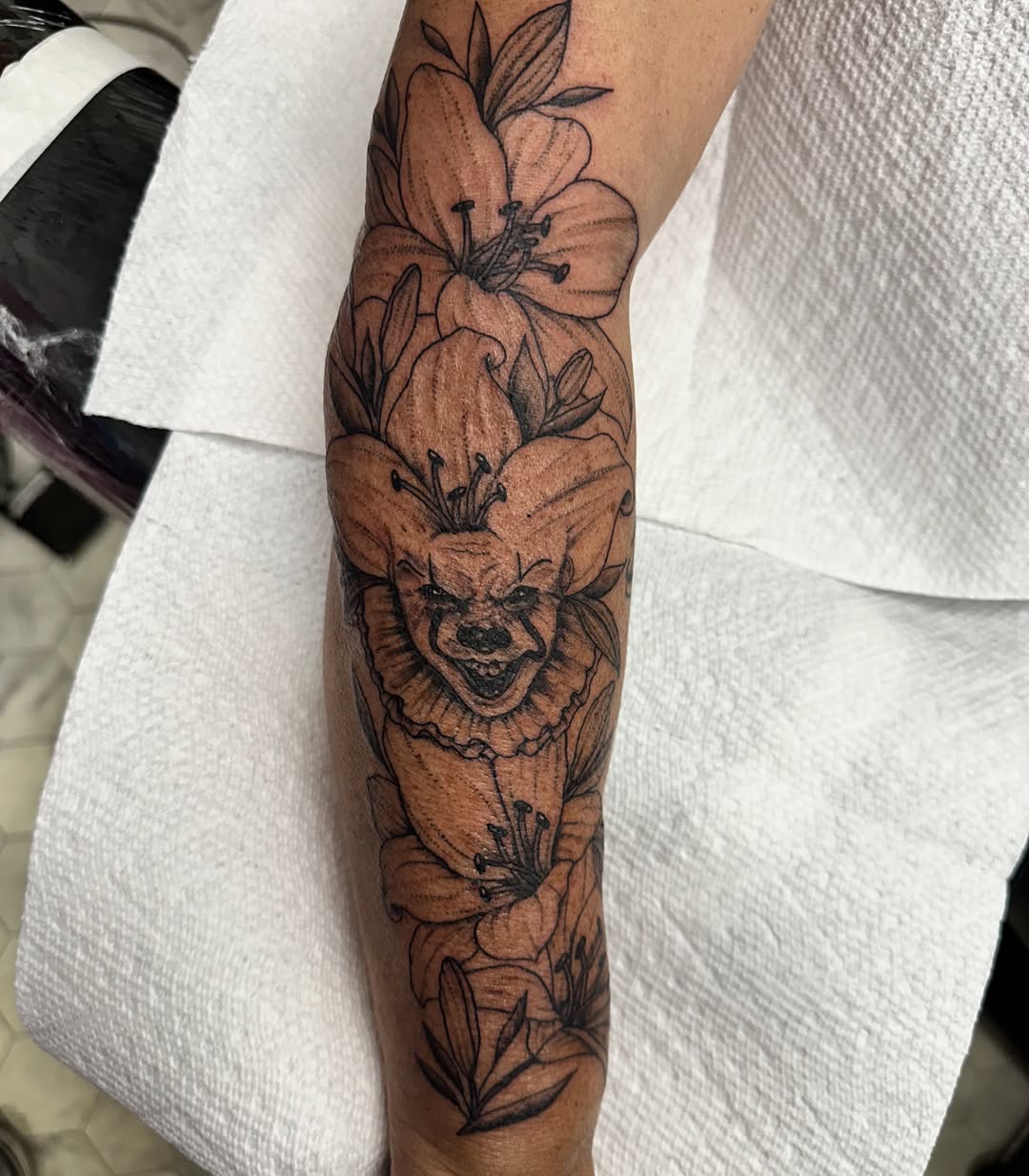 Clown with flowers black and grey tattoo on the forearm by Nicki Hoverson