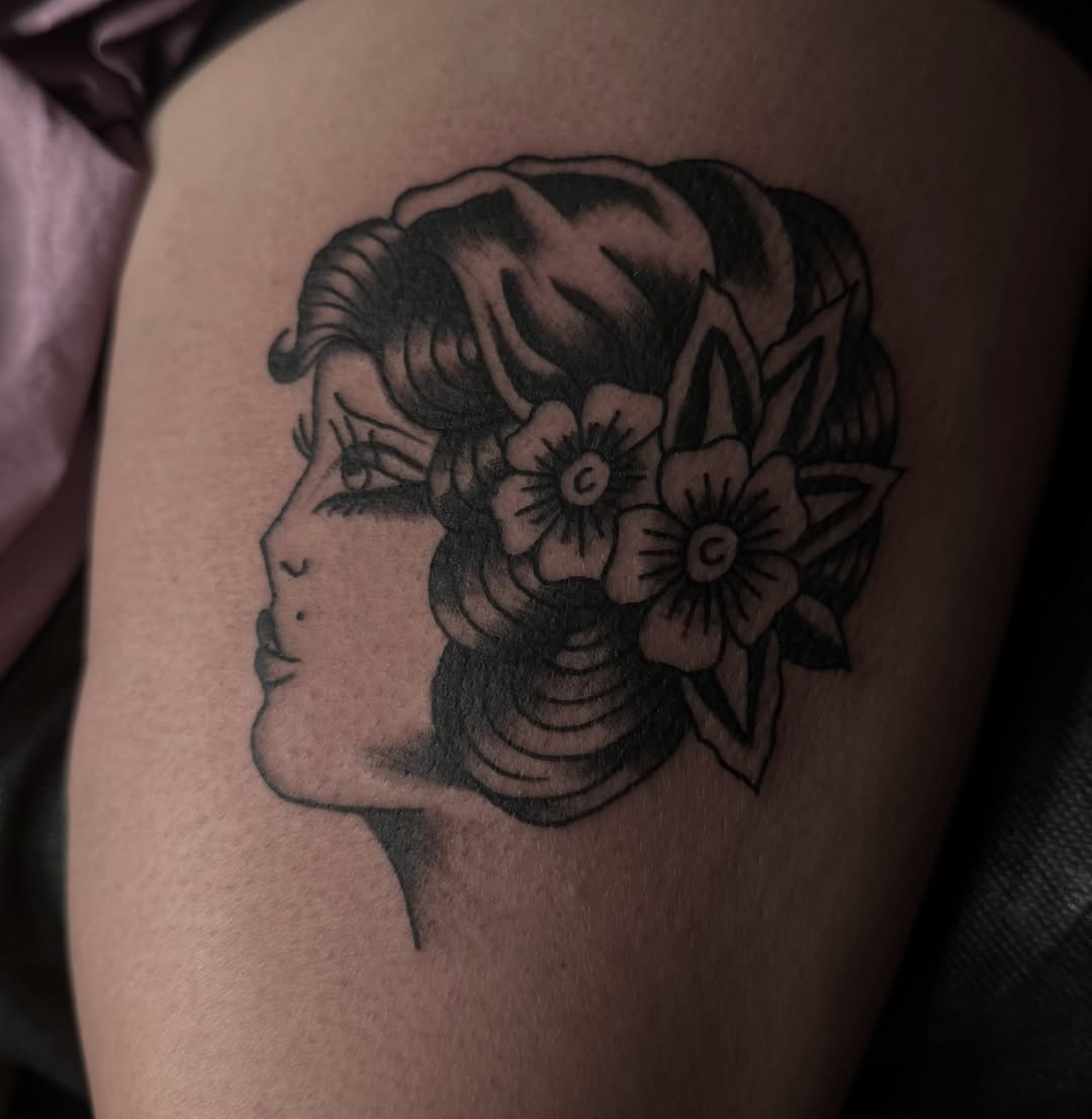 Profile of a woman with flowers black and grey tattoo on the thigh by Jordan Sandoval