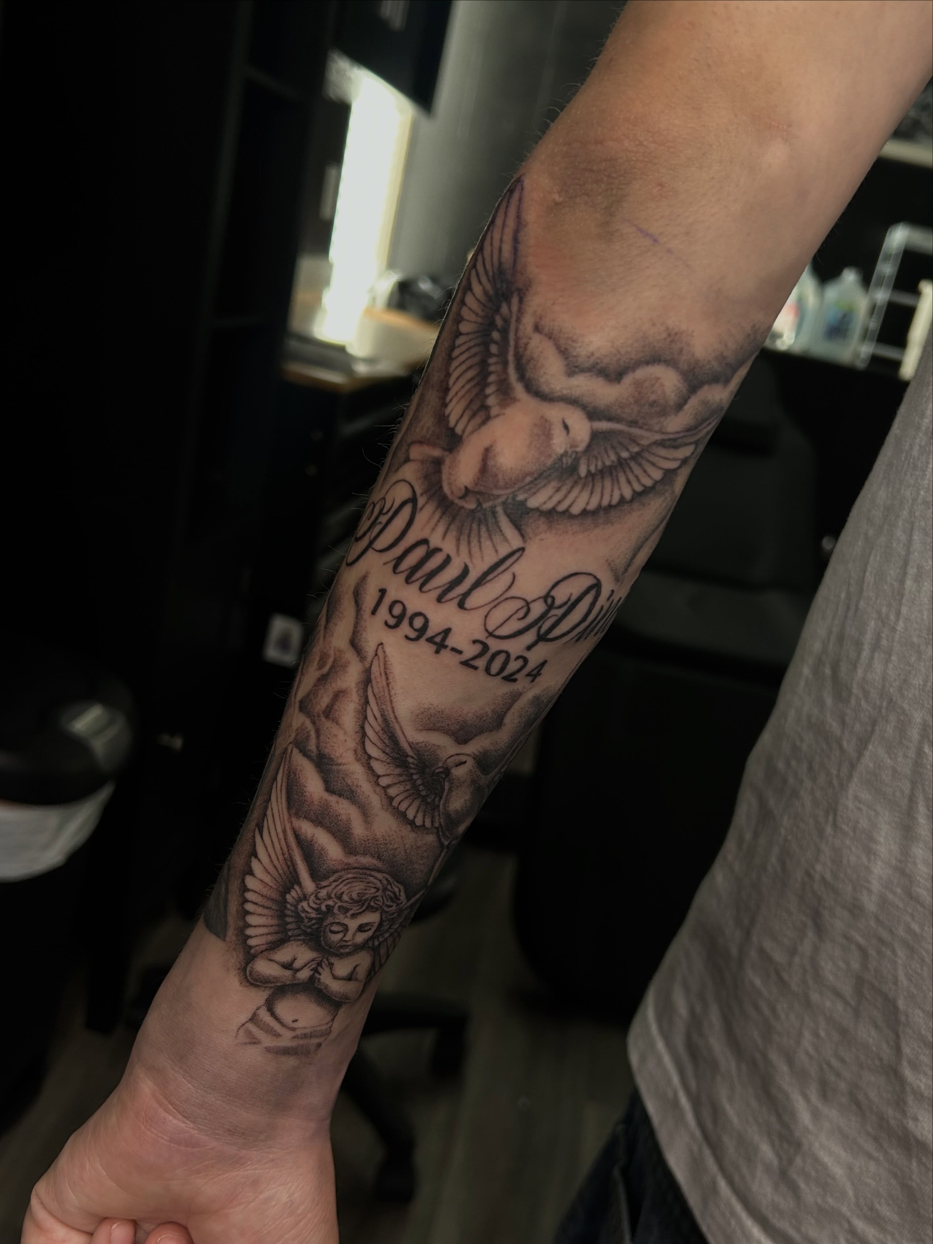 Angels and name black and grey tattoo on the forearm by Ximena Favela