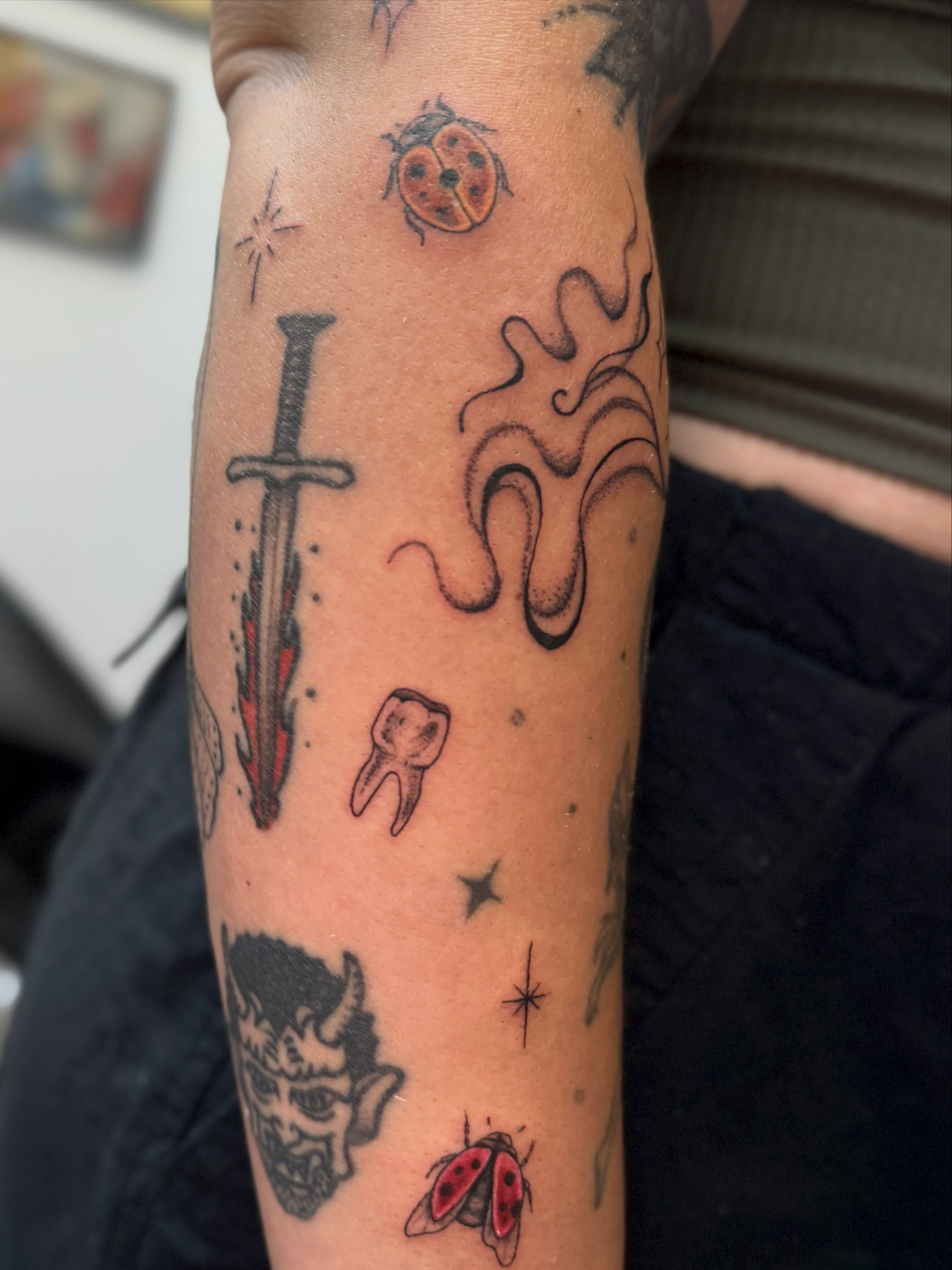 Sword, ladybug, tooth, flame, demon head American traditional tattoo on the forearm by Kamakana Pankiwska