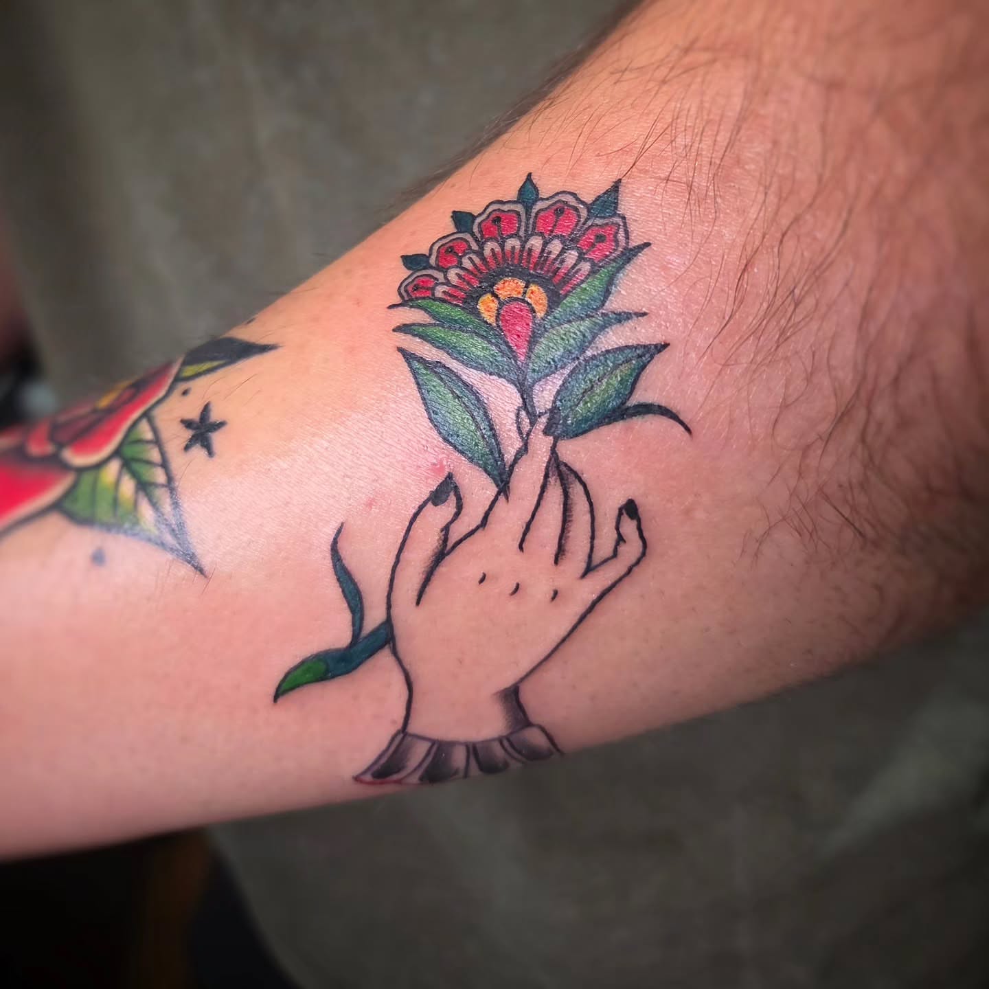 Hand holding flower American traditional tattoo on the forearm by Jam ⚡️🐉🖤