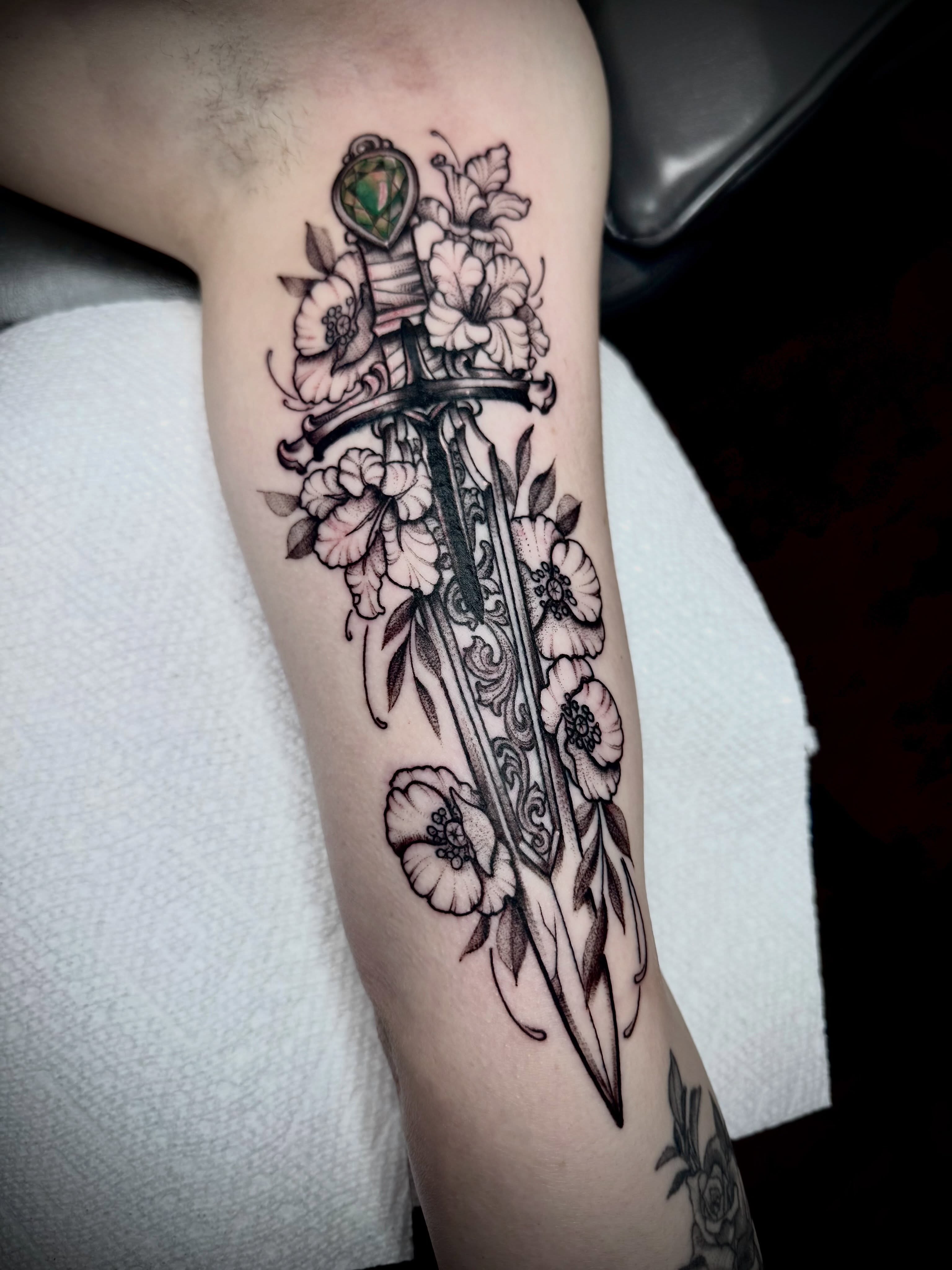 Sword and flowers black and grey tattoo on the forearm by 🏵
