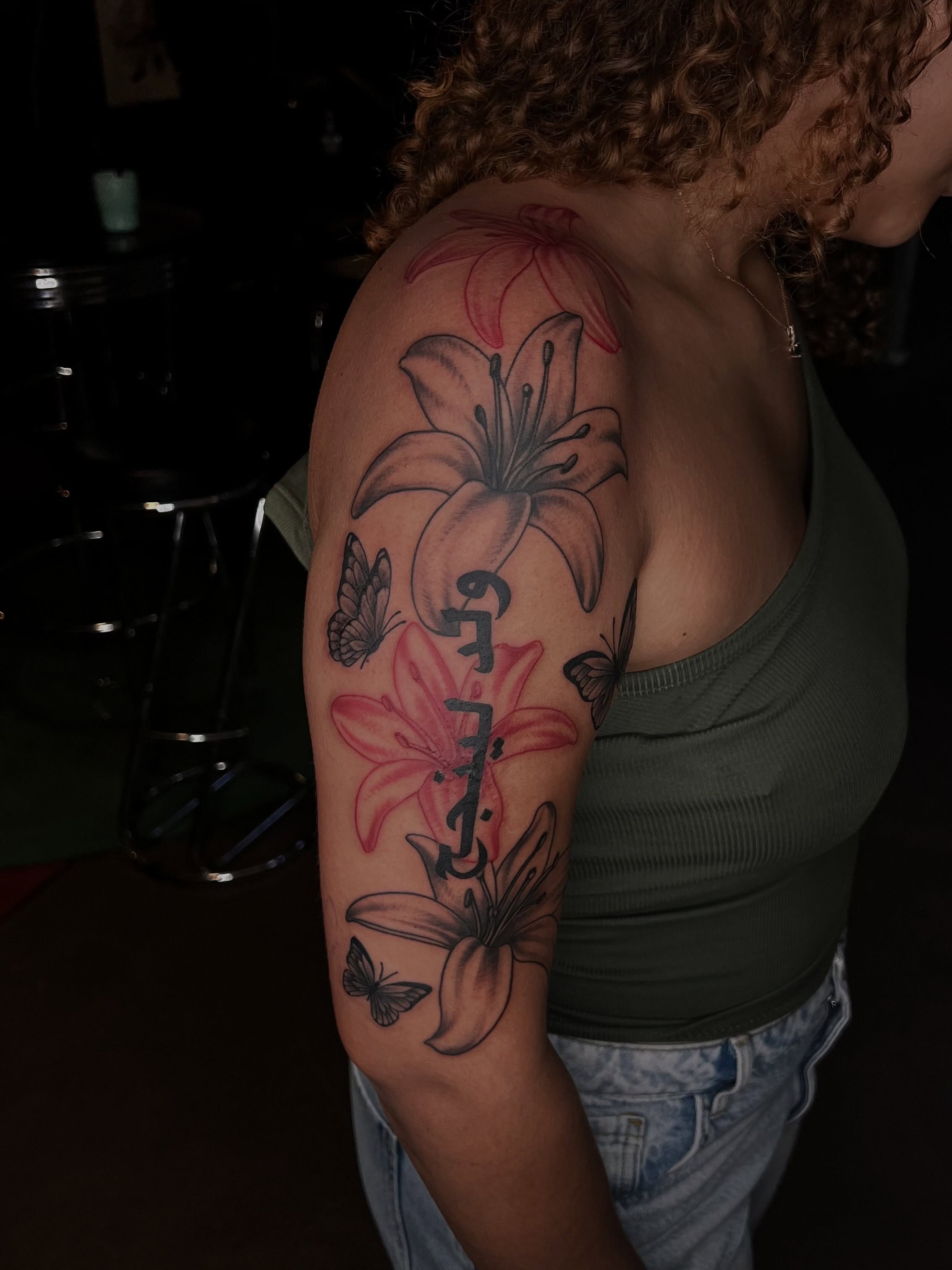 Lilies and butterflies black and grey tattoo on the upper arm by Tattoo (Réaliste), Toulouse, Occitanie