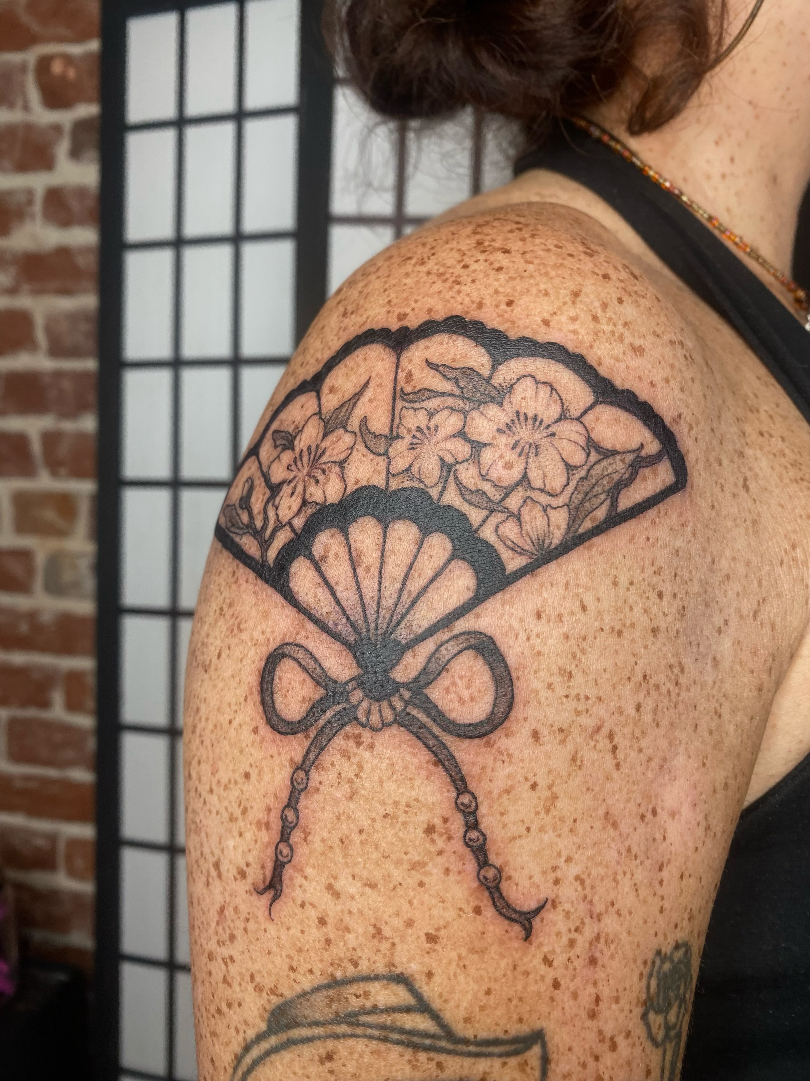 Fan with flowers black and grey tattoo on the shoulder by sarah 🗝️