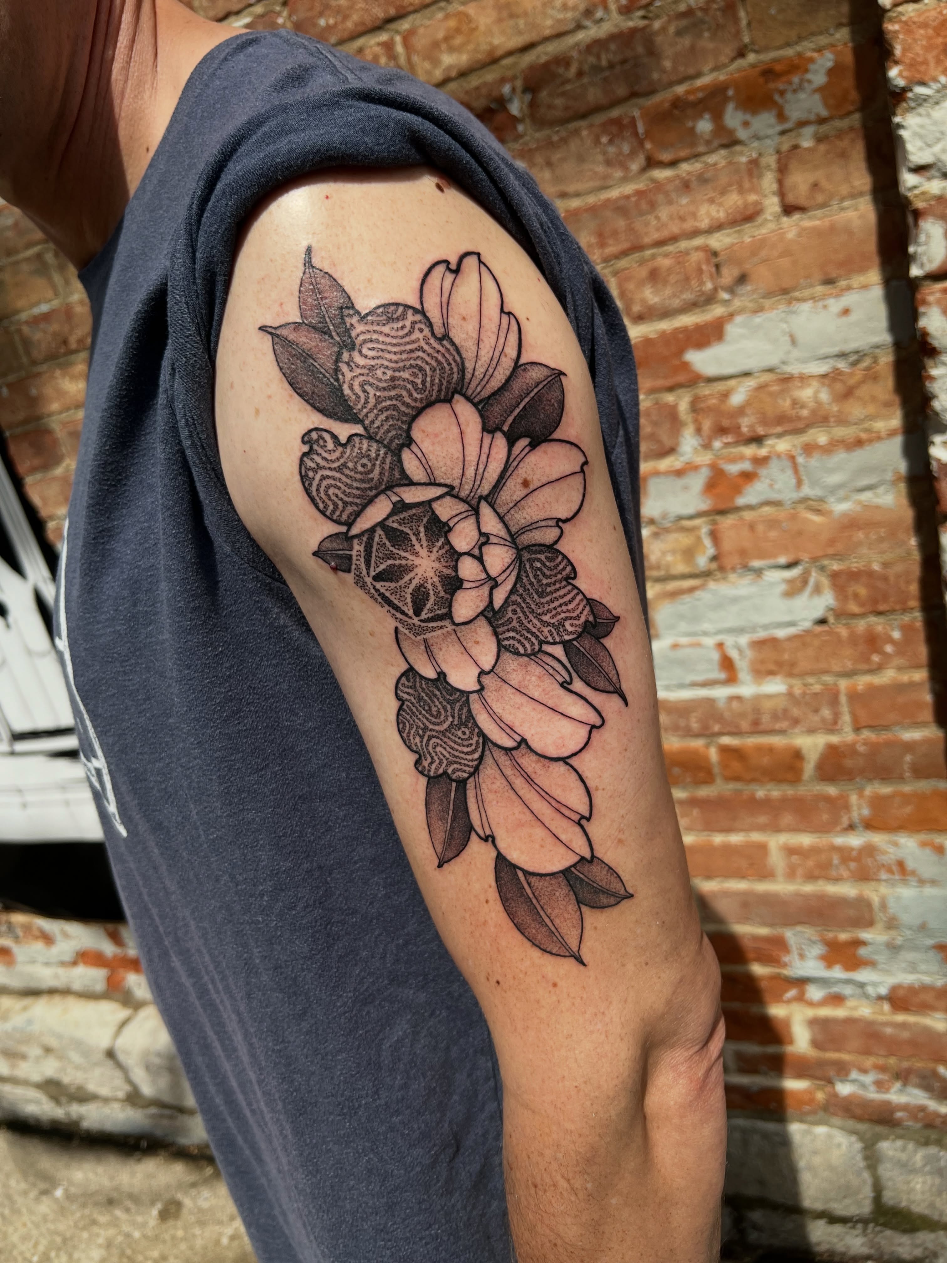 Floral arrangement black and grey tattoo on the upper arm by Riley