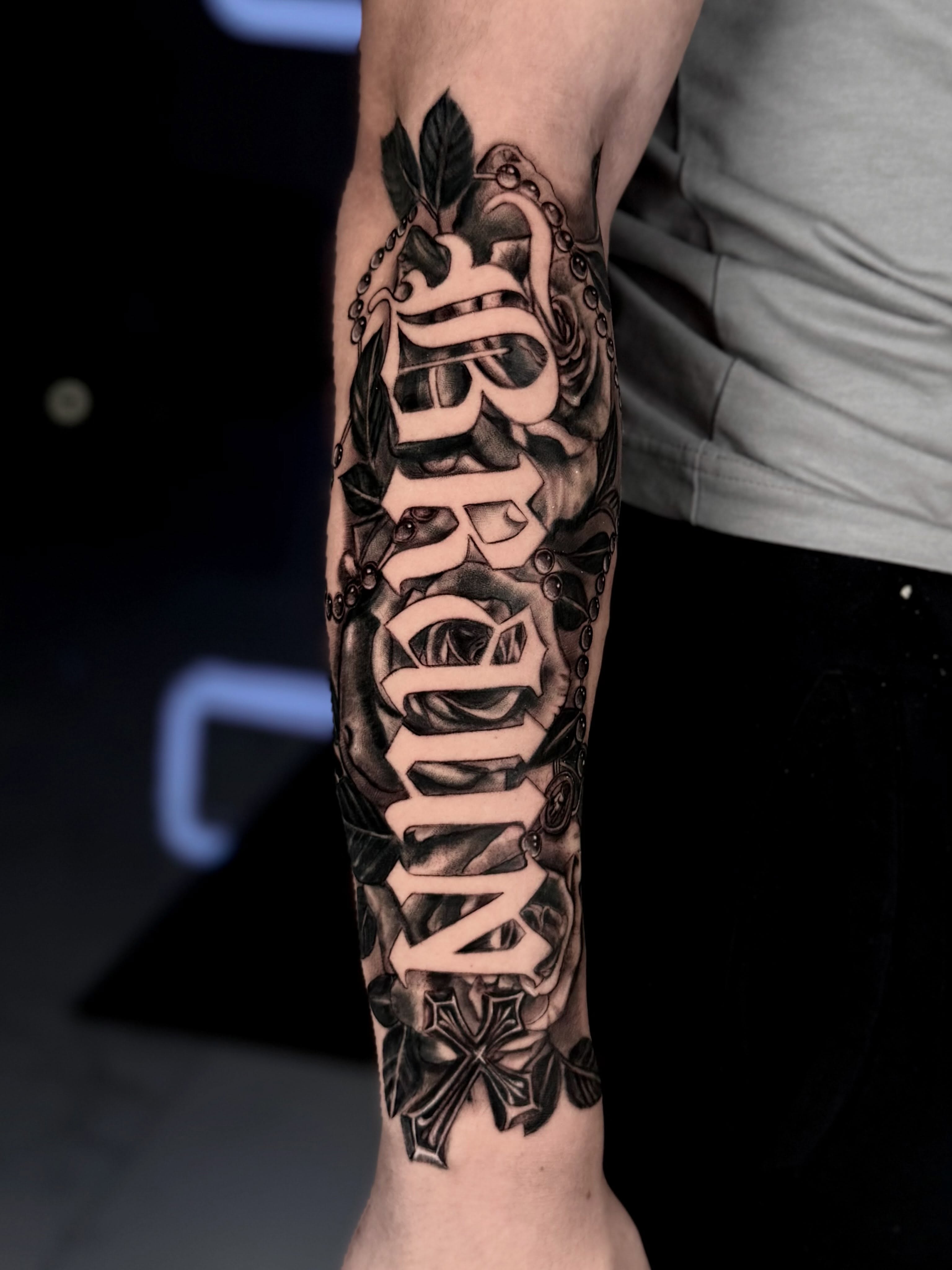 Name with floral and cross lettering script tattoo on the forearm by Idalia Pulido