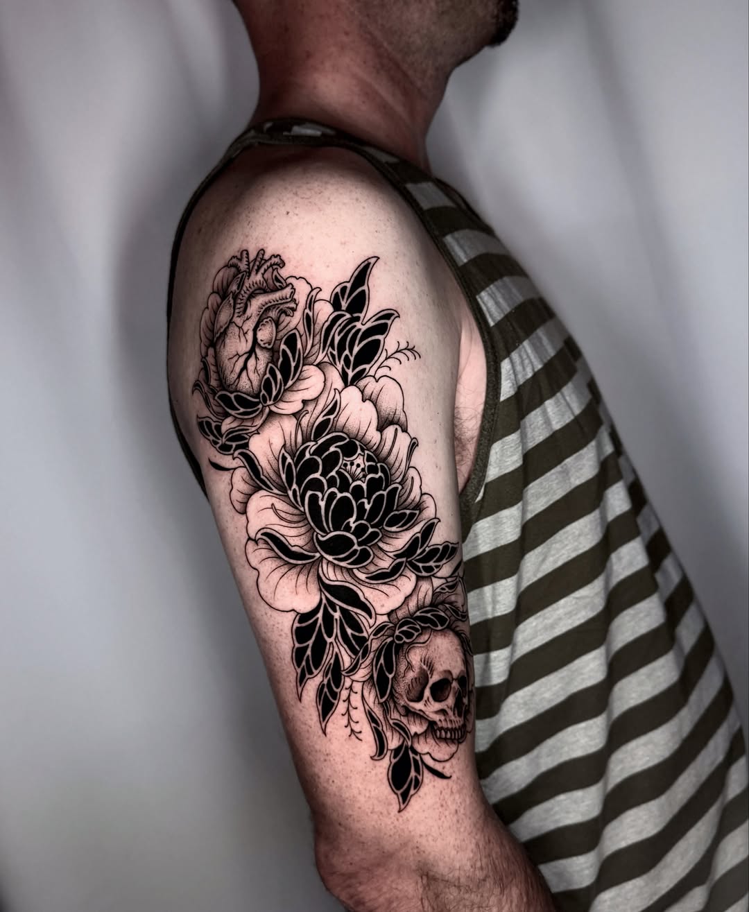Floral arrangement with skull realism tattoo on the upper arm by Kathryn Semus