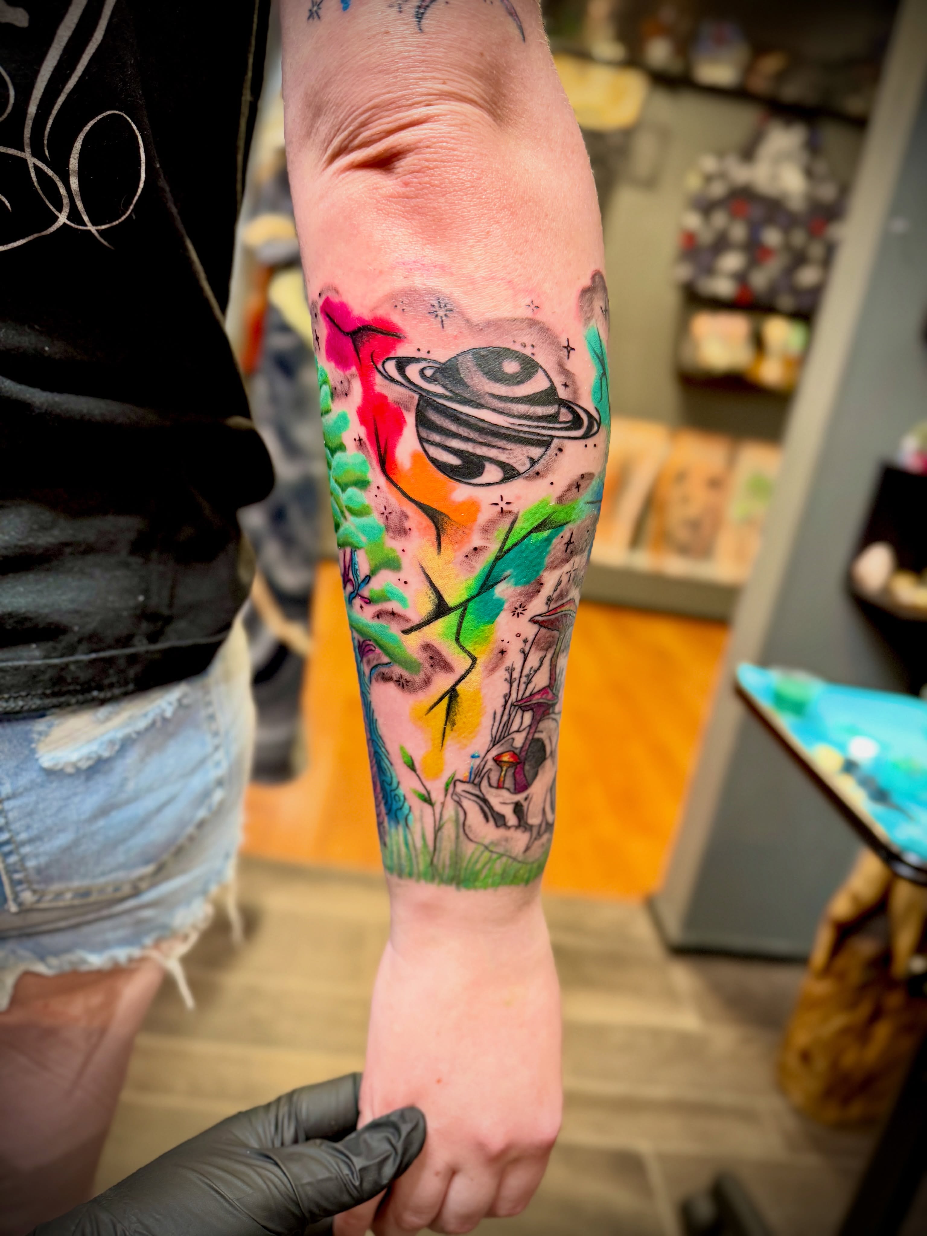 Space-themed landscape watercolor tattoo on the forearm by Kacy Blalock