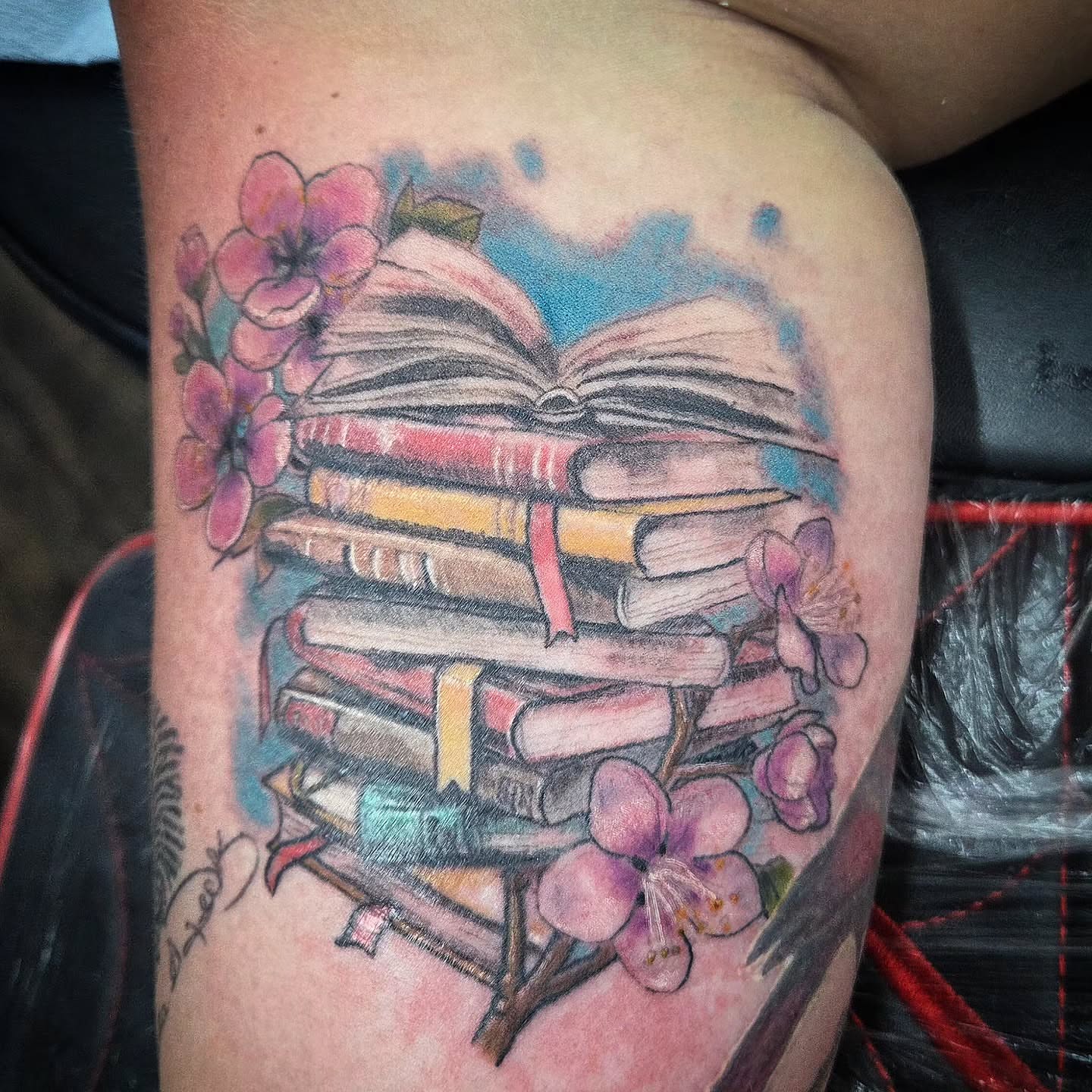 Stack of books and flowers watercolor tattoo on the thigh by Matthew Todd Kremer