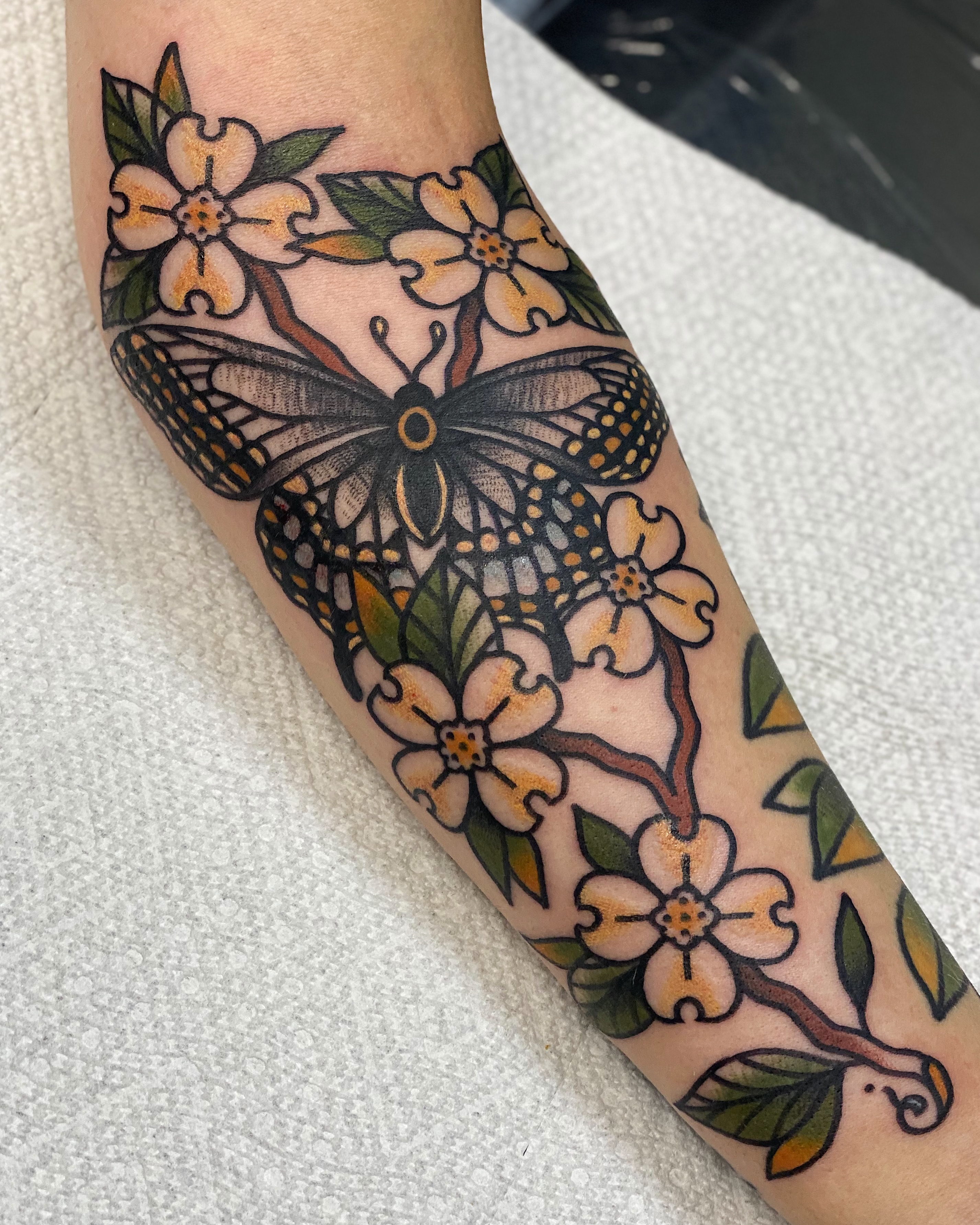 Butterfly and flowers American traditional tattoo on the forearm by Dakota Amato