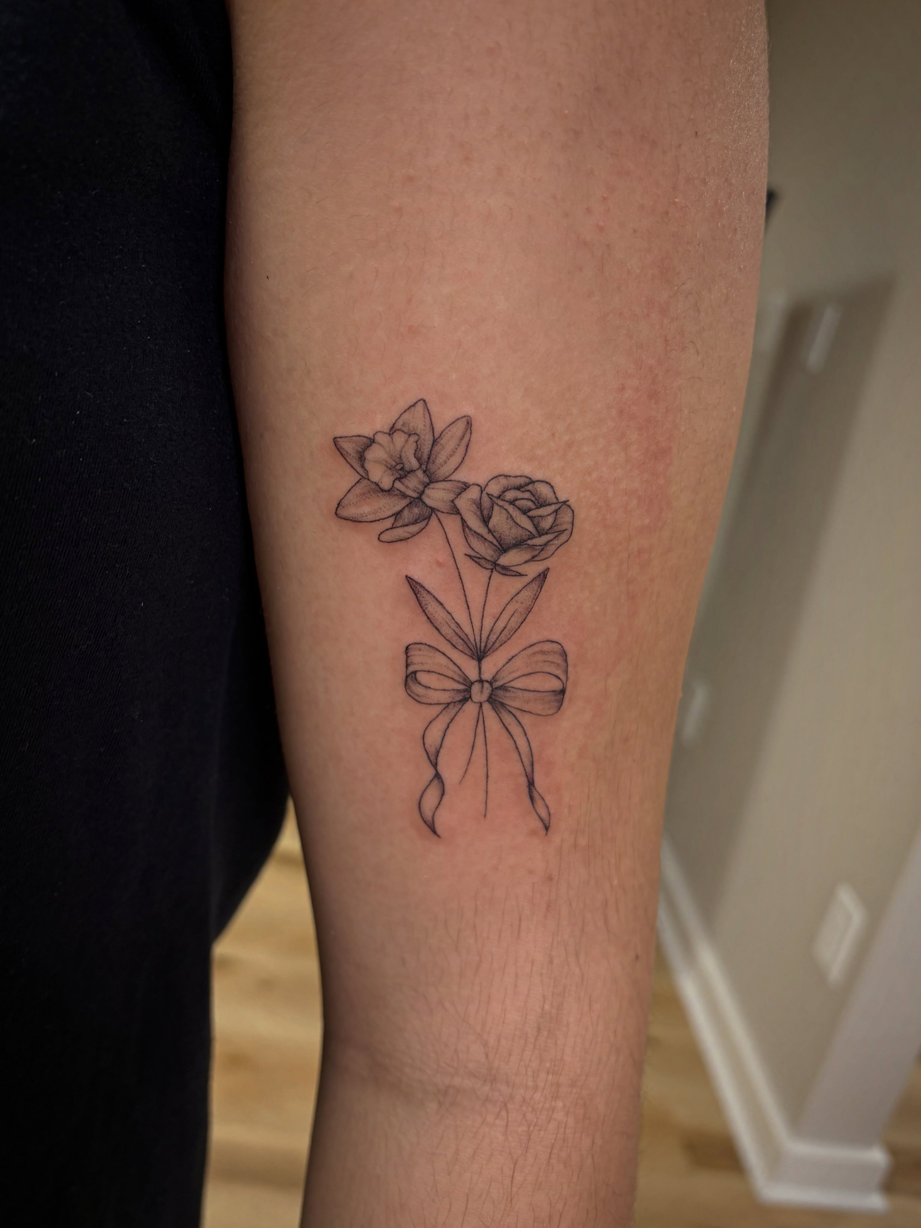 Flowers and bow black and grey tattoo on the forearm by Francesca Siwa