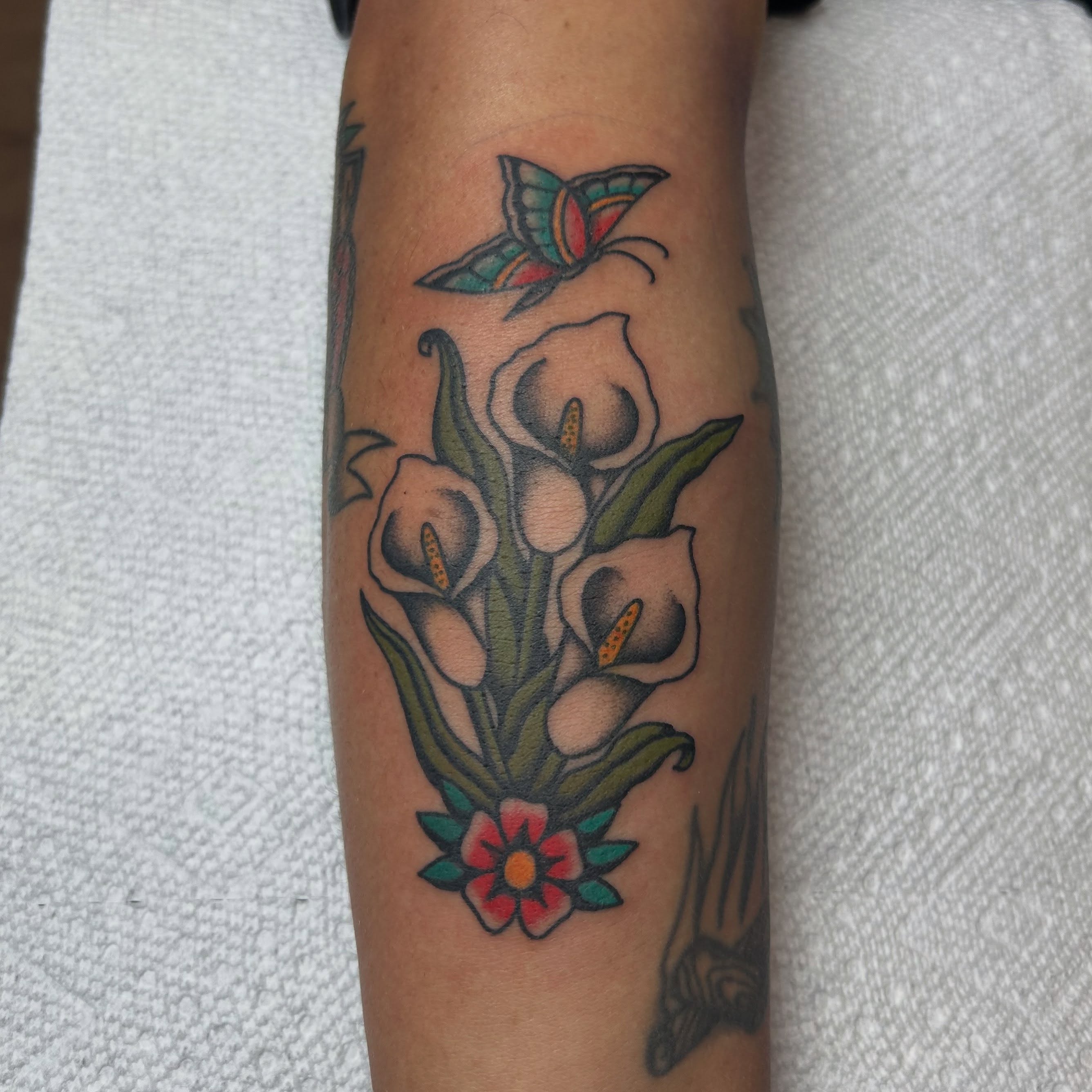 Calla lilies and butterfly American traditional tattoo on the forearm by Stephen Sanchez