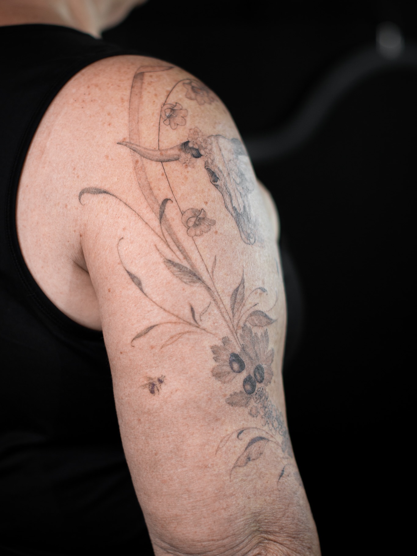 Bull skull and floral black and grey tattoo on the upper arm by Aries Rising