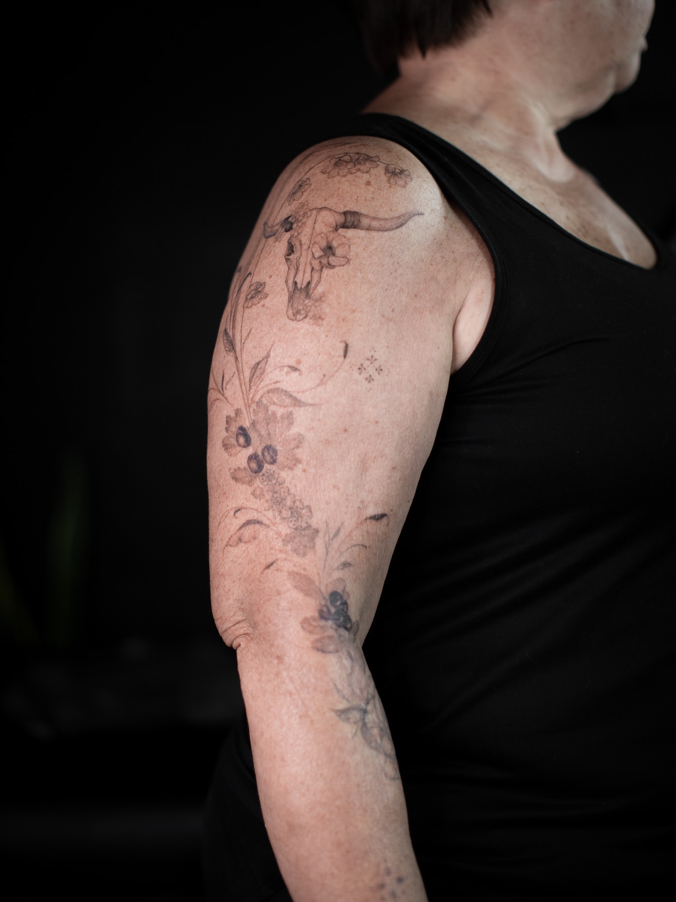 Bull skull with floral patterns black and grey tattoo on the upper arm by Aries Rising