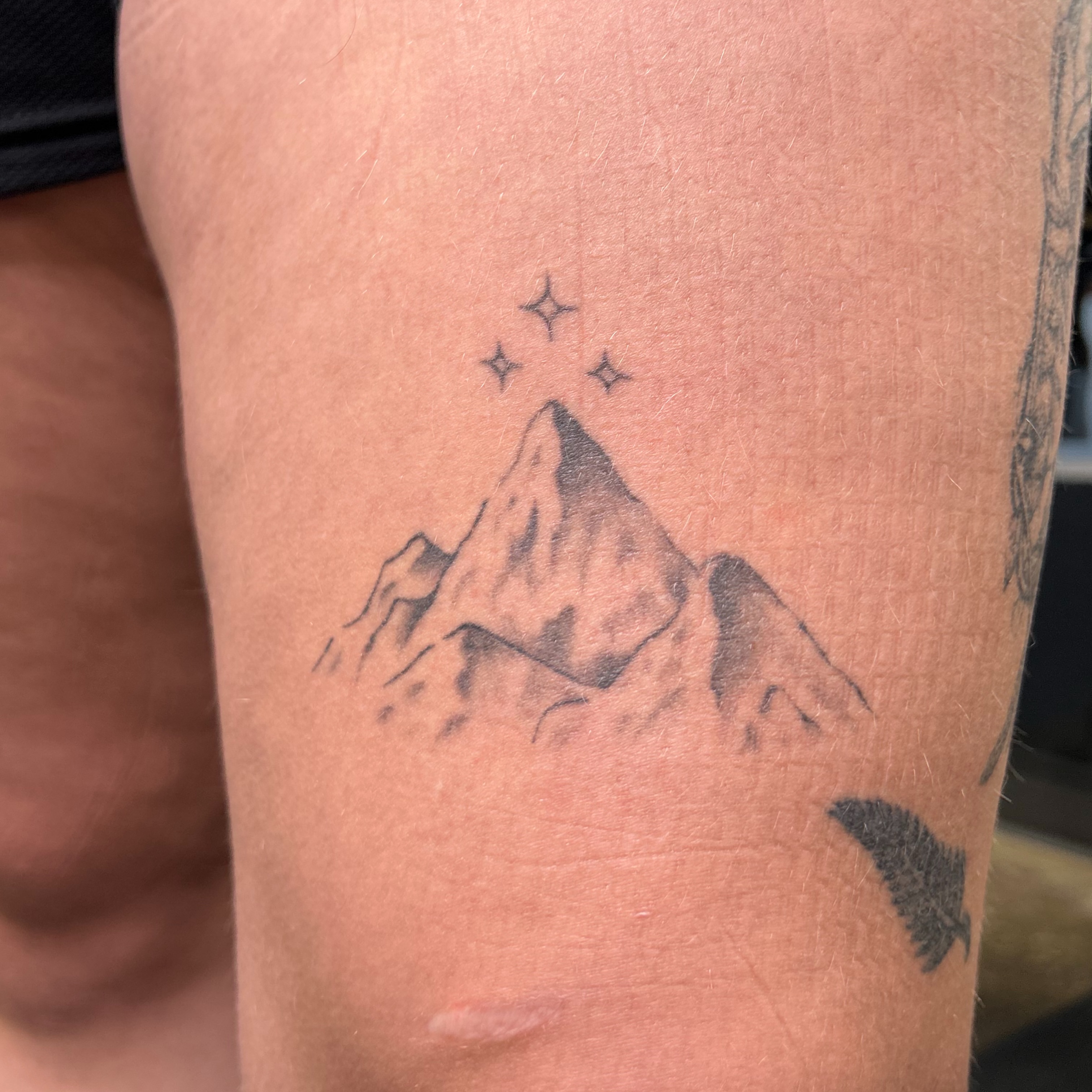 Mountain peak with stars black and grey tattoo on the thigh by Natalie Johnson, Minneapolis, Minnesota