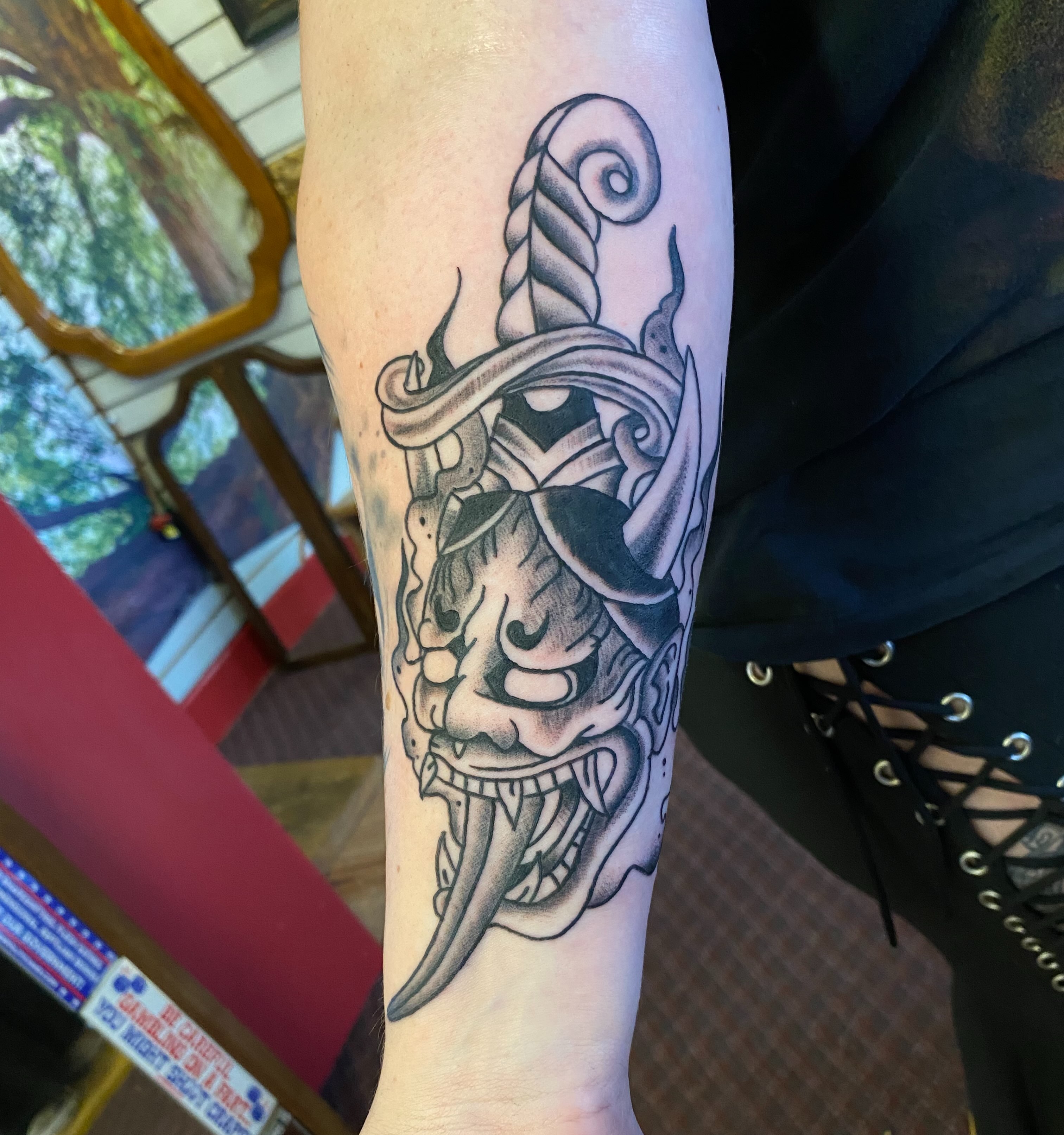 Mask with sword black and grey tattoo on the forearm by Tommy O'Connell