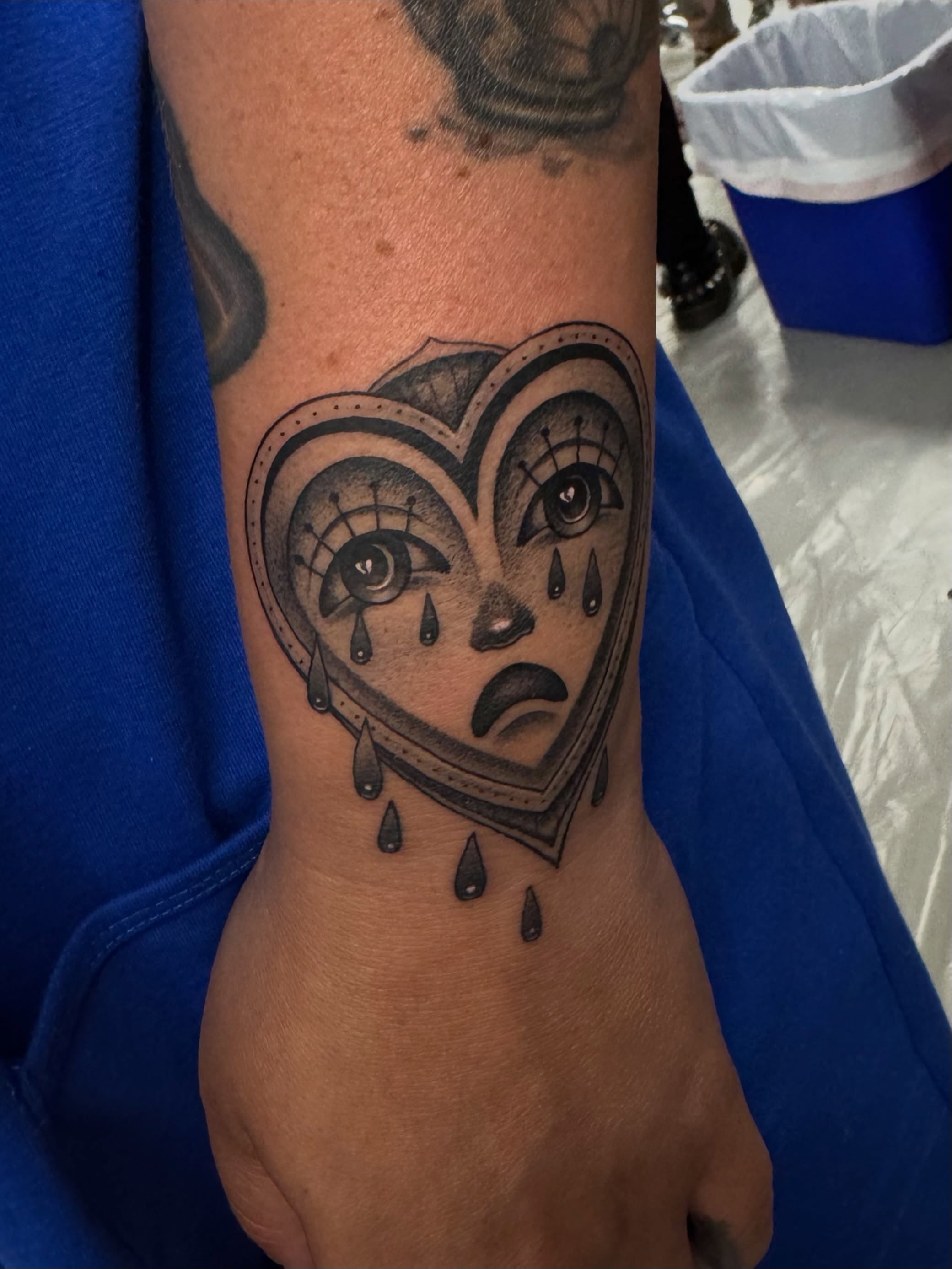 Heart with crying face black and grey tattoo on the forearm by Caroline Yurek