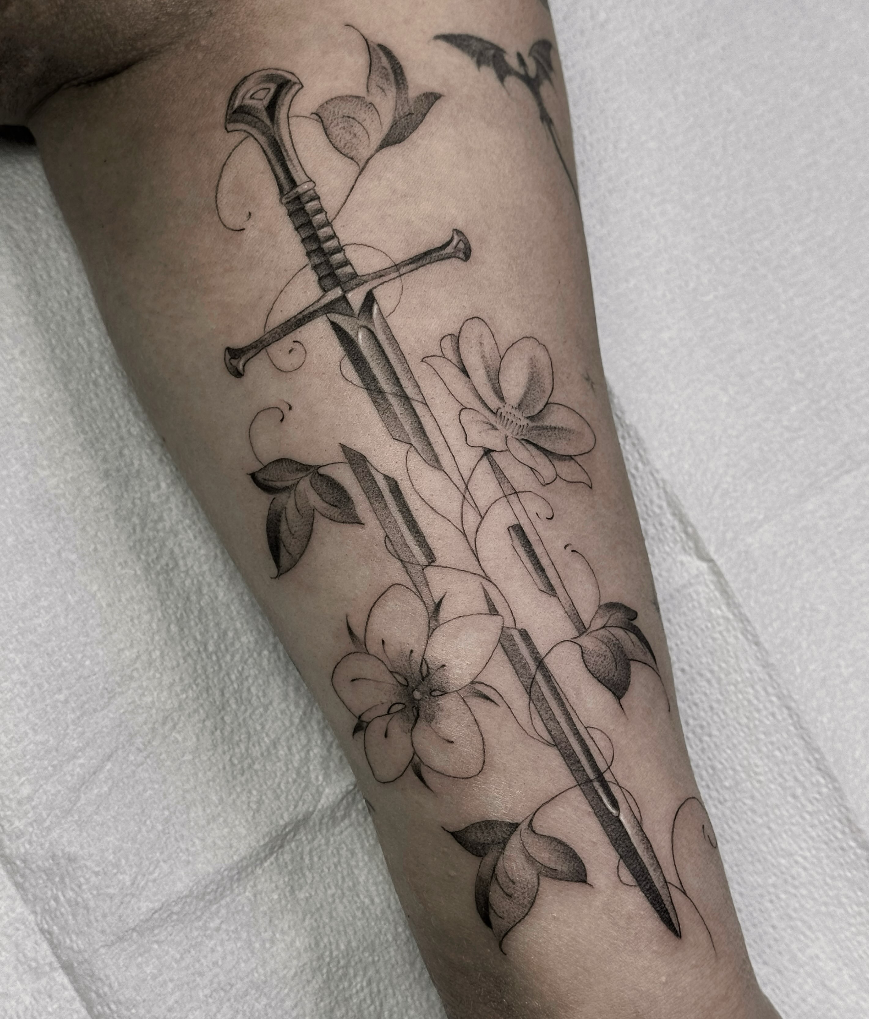 Crossed swords and flowers black and grey tattoo on the leg by Alyssa . Villela