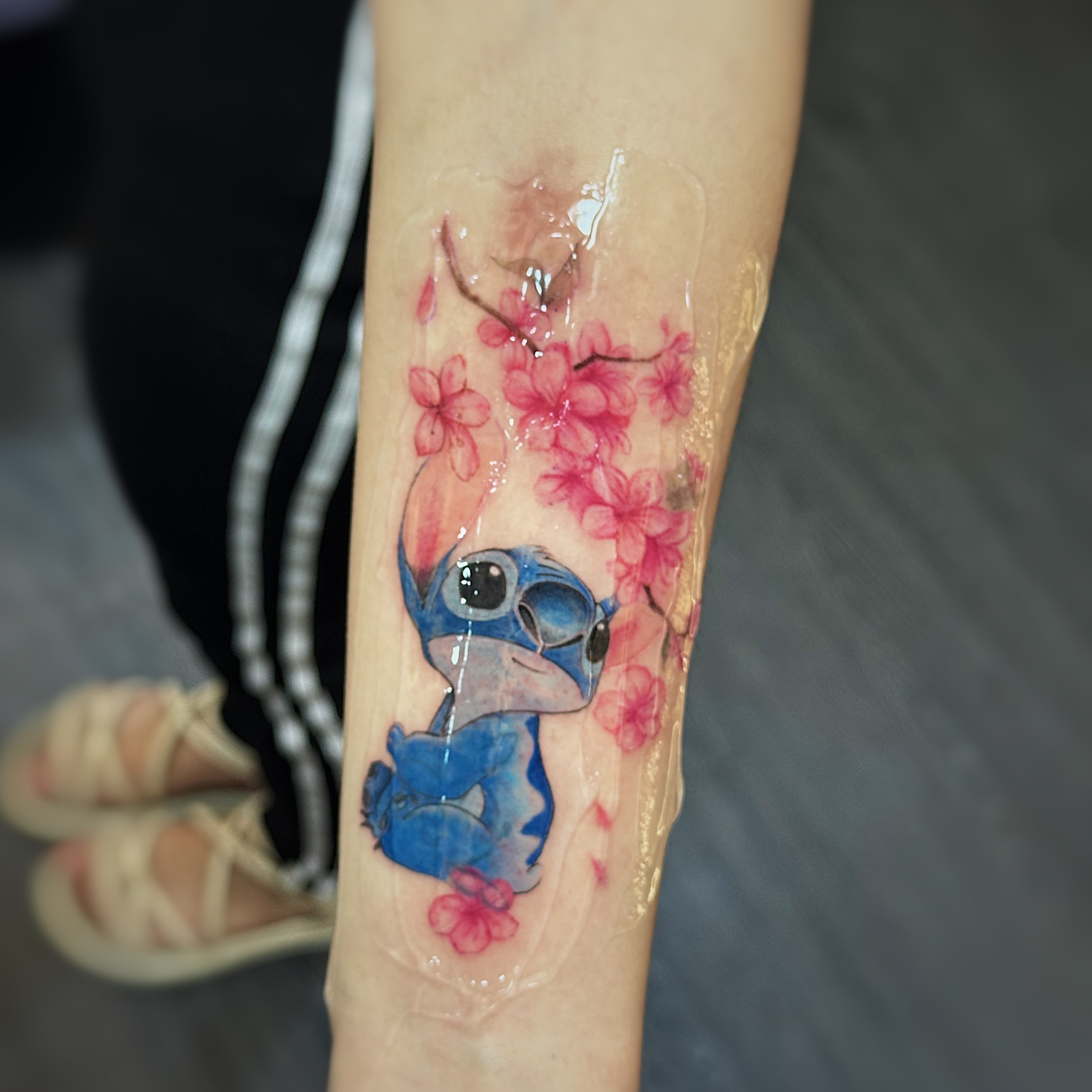 Stitch and cherry blossoms watercolor tattoo on the forearm by 墨匠紋身|新店店, New Taipei City