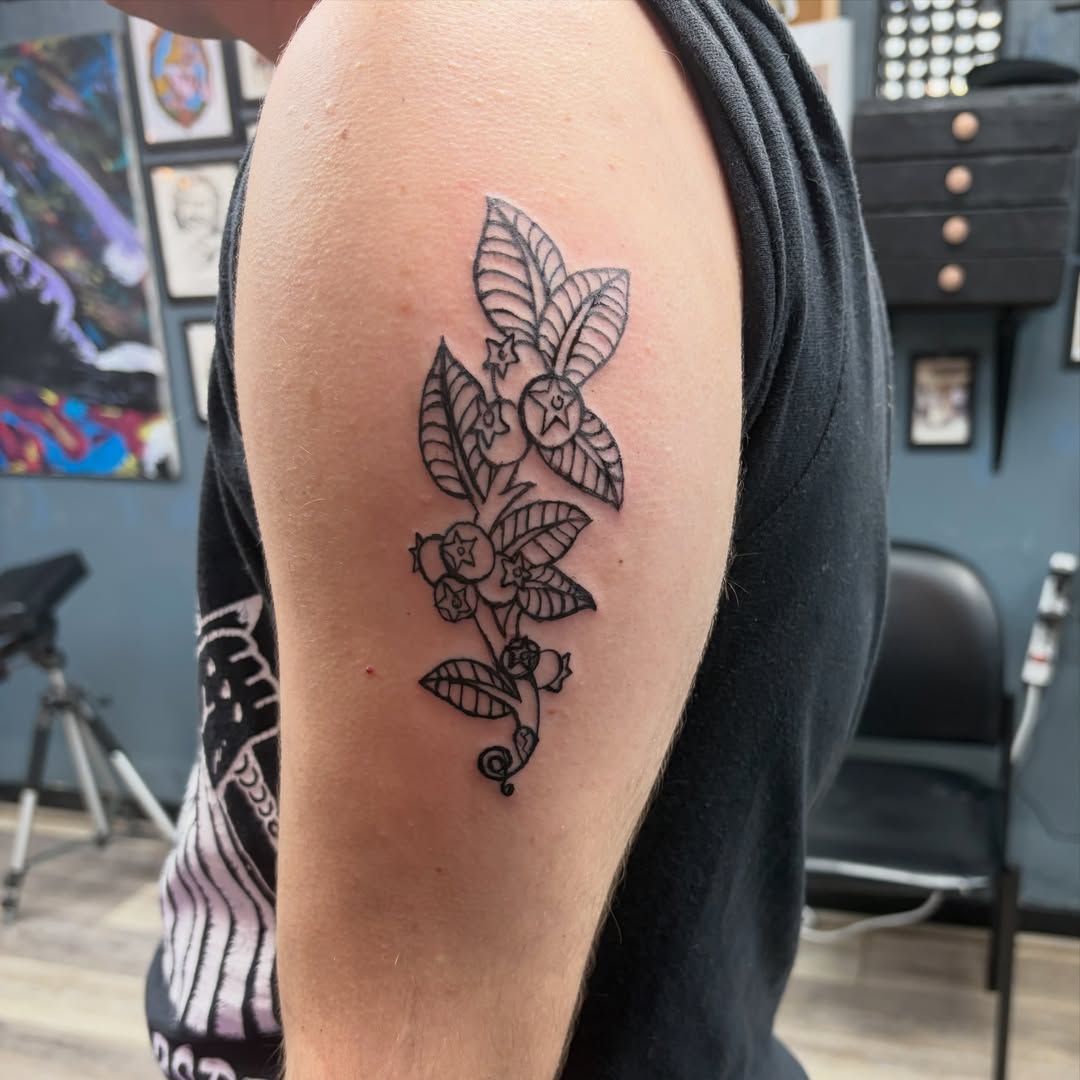 Blueberry plant black and grey tattoo on the upper arm by Madison