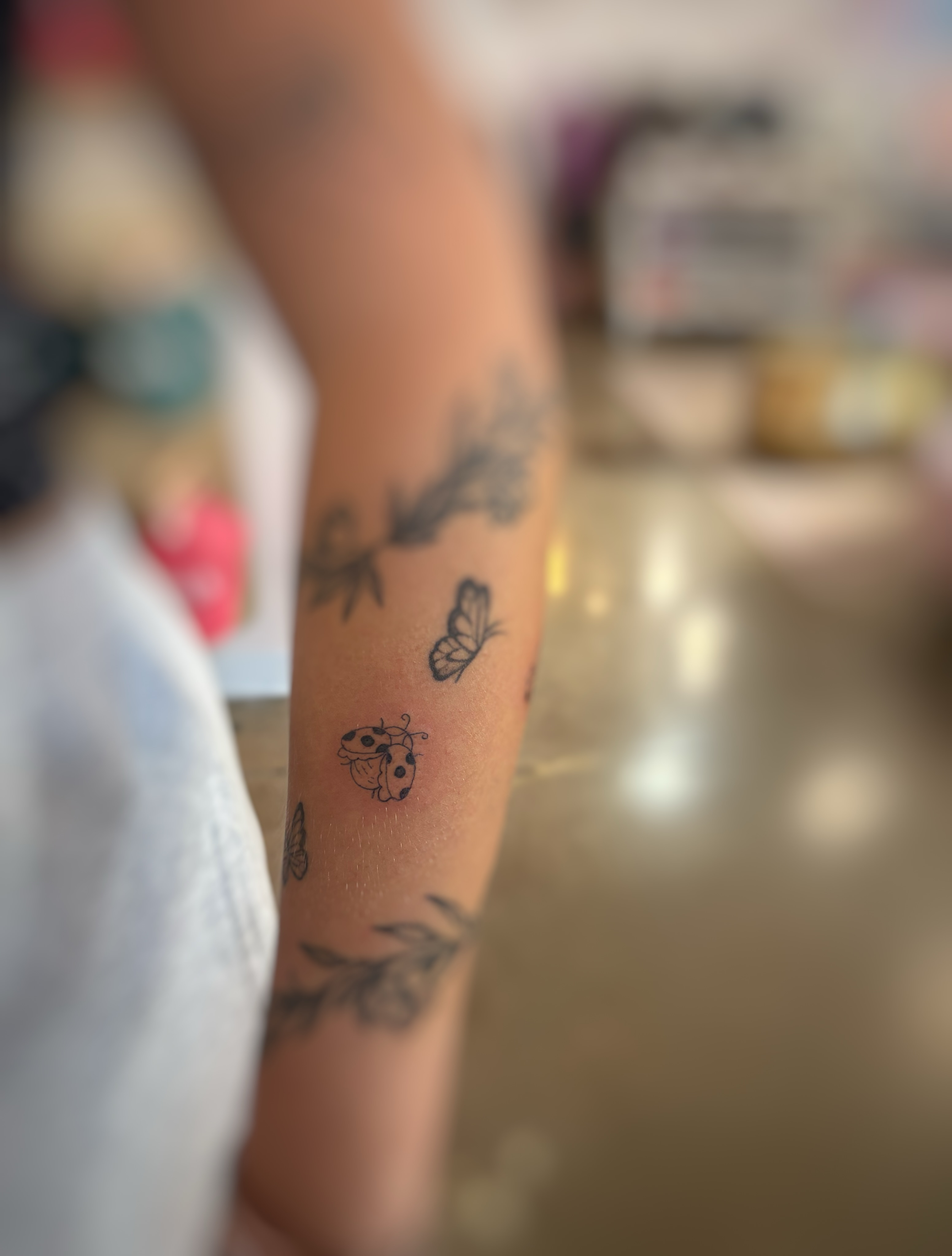 Butterfly and ladybug black and grey tattoo on the forearm by Holly