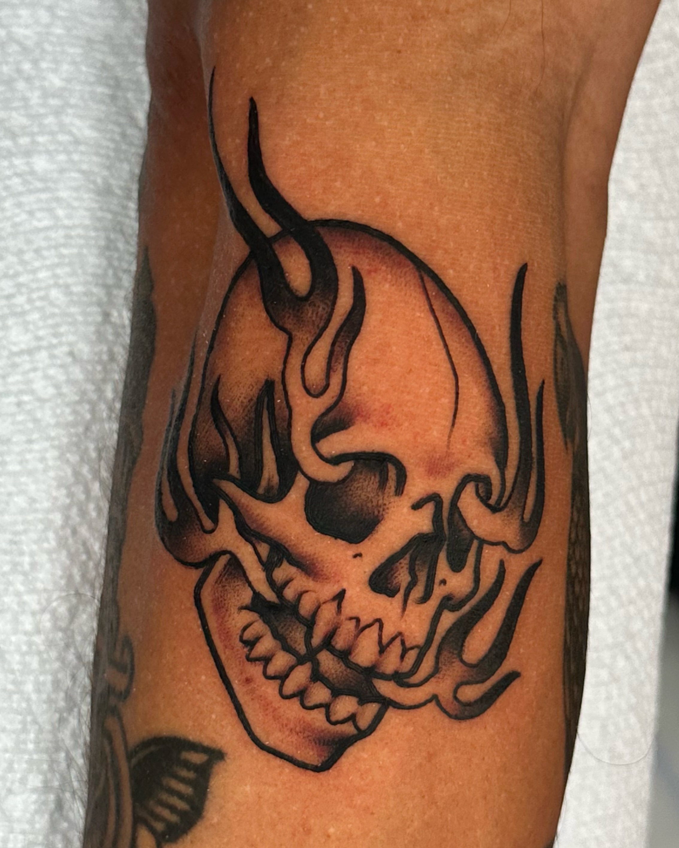 Flaming skull black and grey tattoo on the forearm by Big Nance