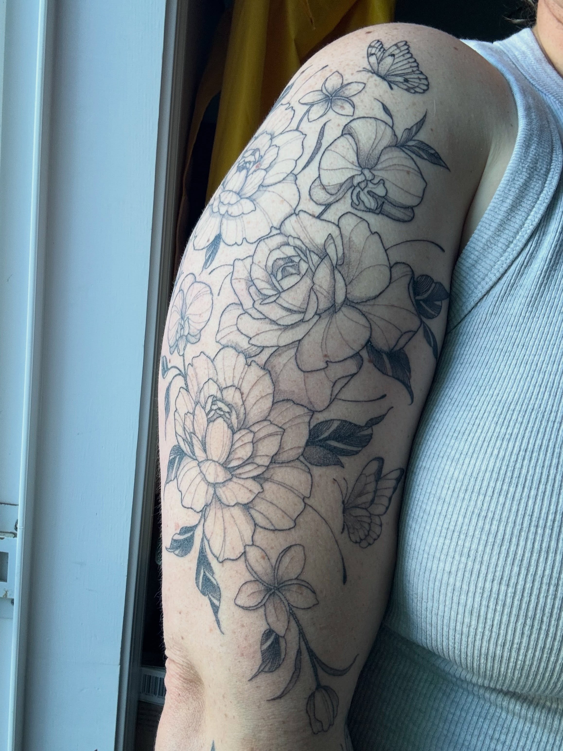 Floral bouquet black and grey tattoo on the upper arm by Lo Gwynn