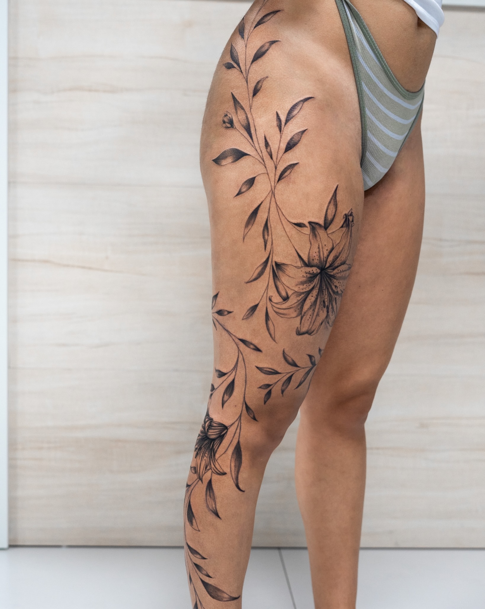 Floral vine black and grey tattoo on the thigh by The Tattoo Plug