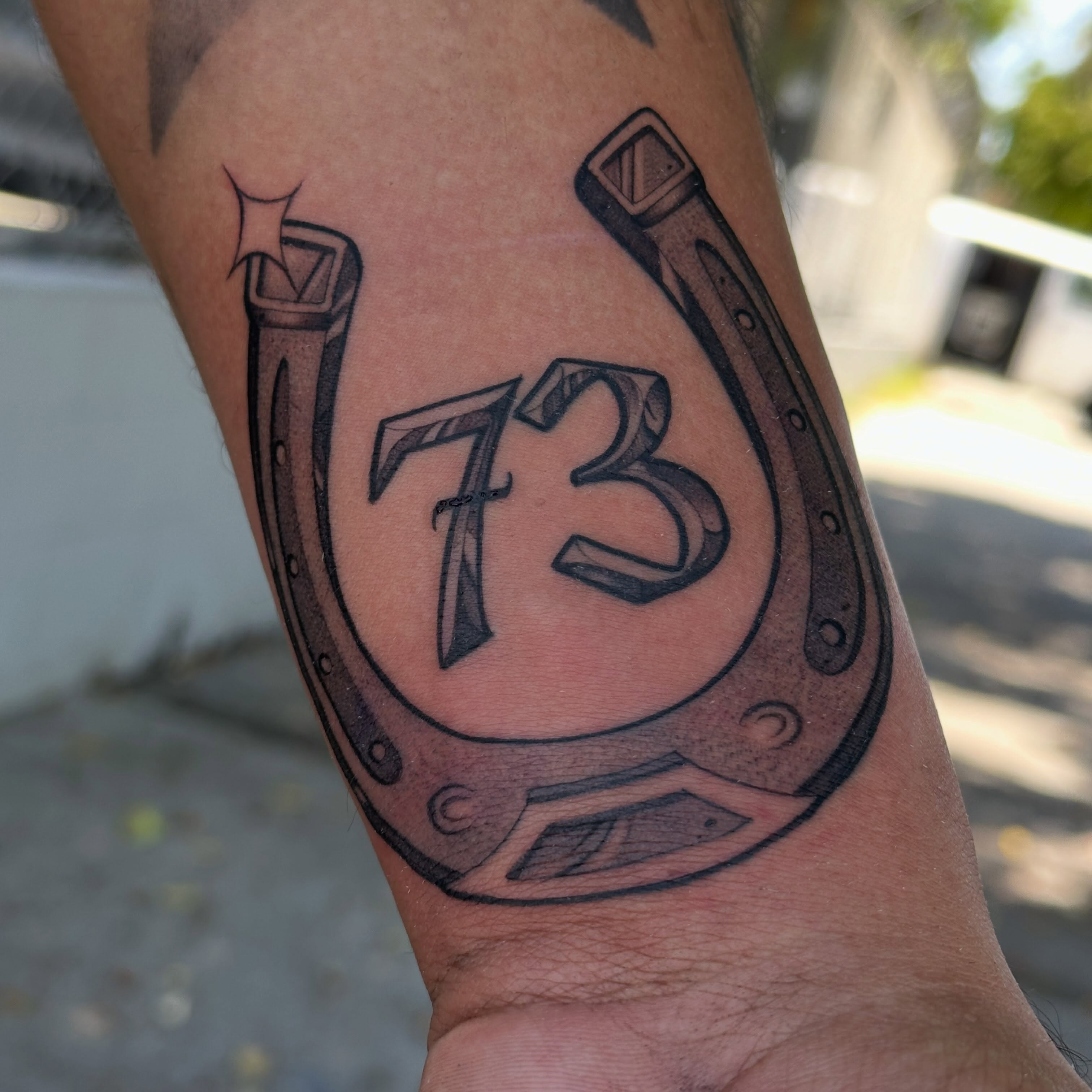 Horseshoe with number 73 black and grey tattoo on the forearm by San Diego Tattoo Artist