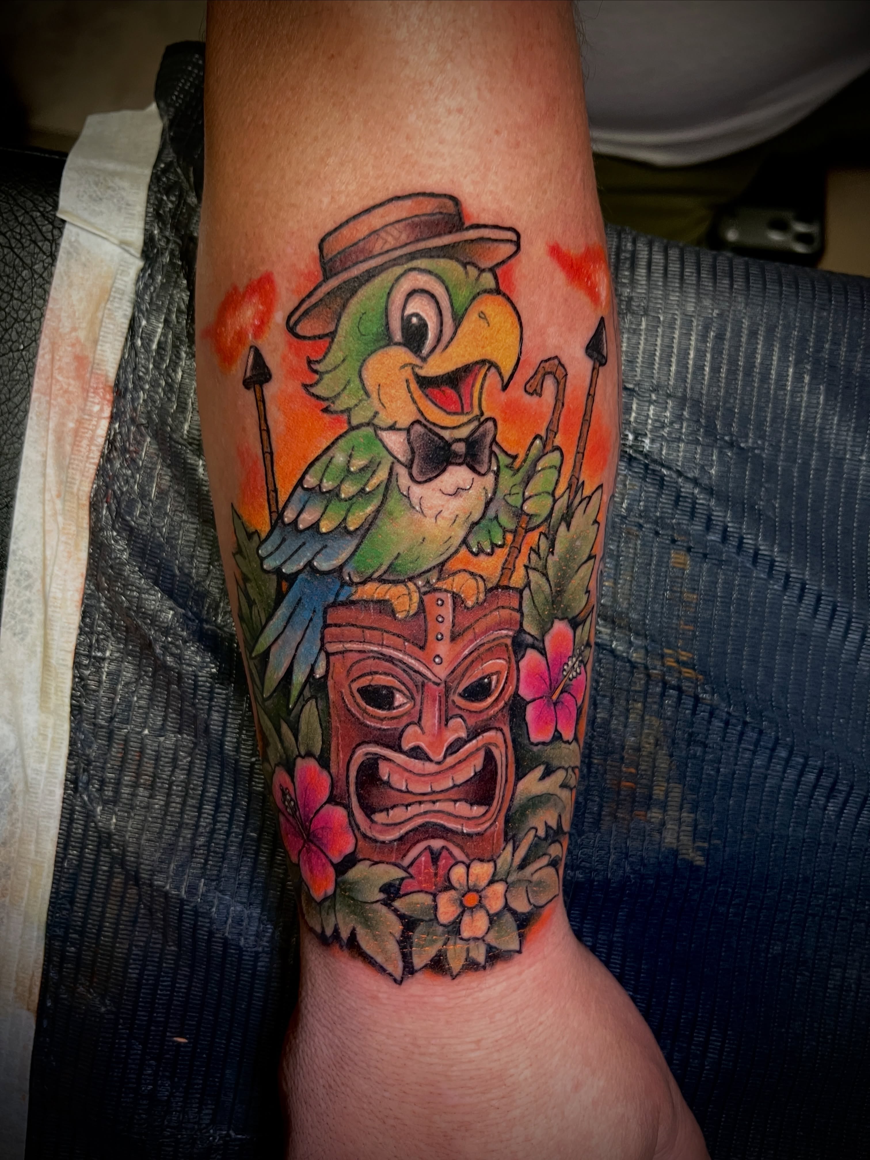 Parrot and tiki mask American traditional tattoo on the forearm by 🗿🌴TᗩᕼITI GIᒪ✨🏰