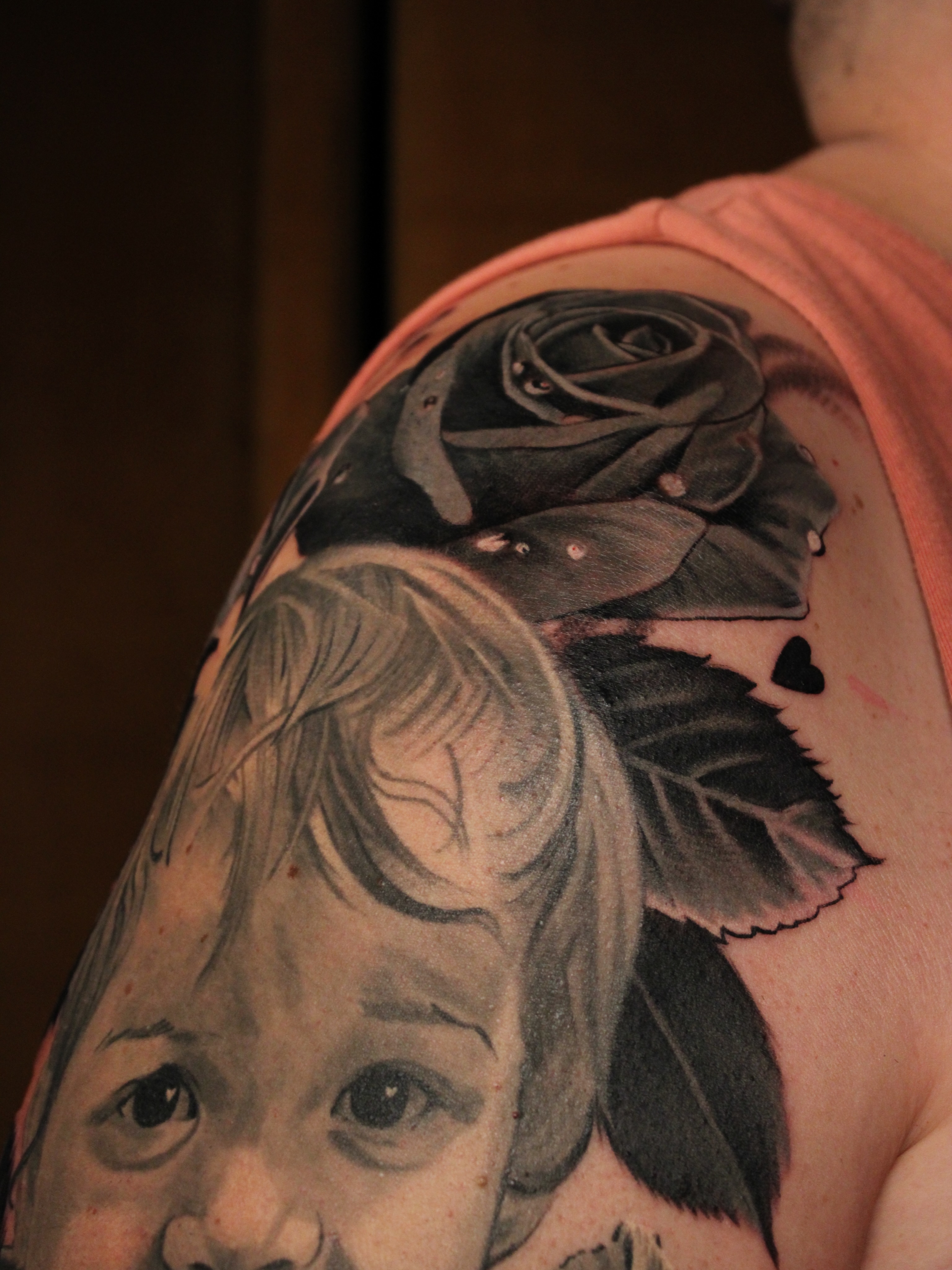 Child's face with rose realism tattoo on the shoulder by Eva Williams