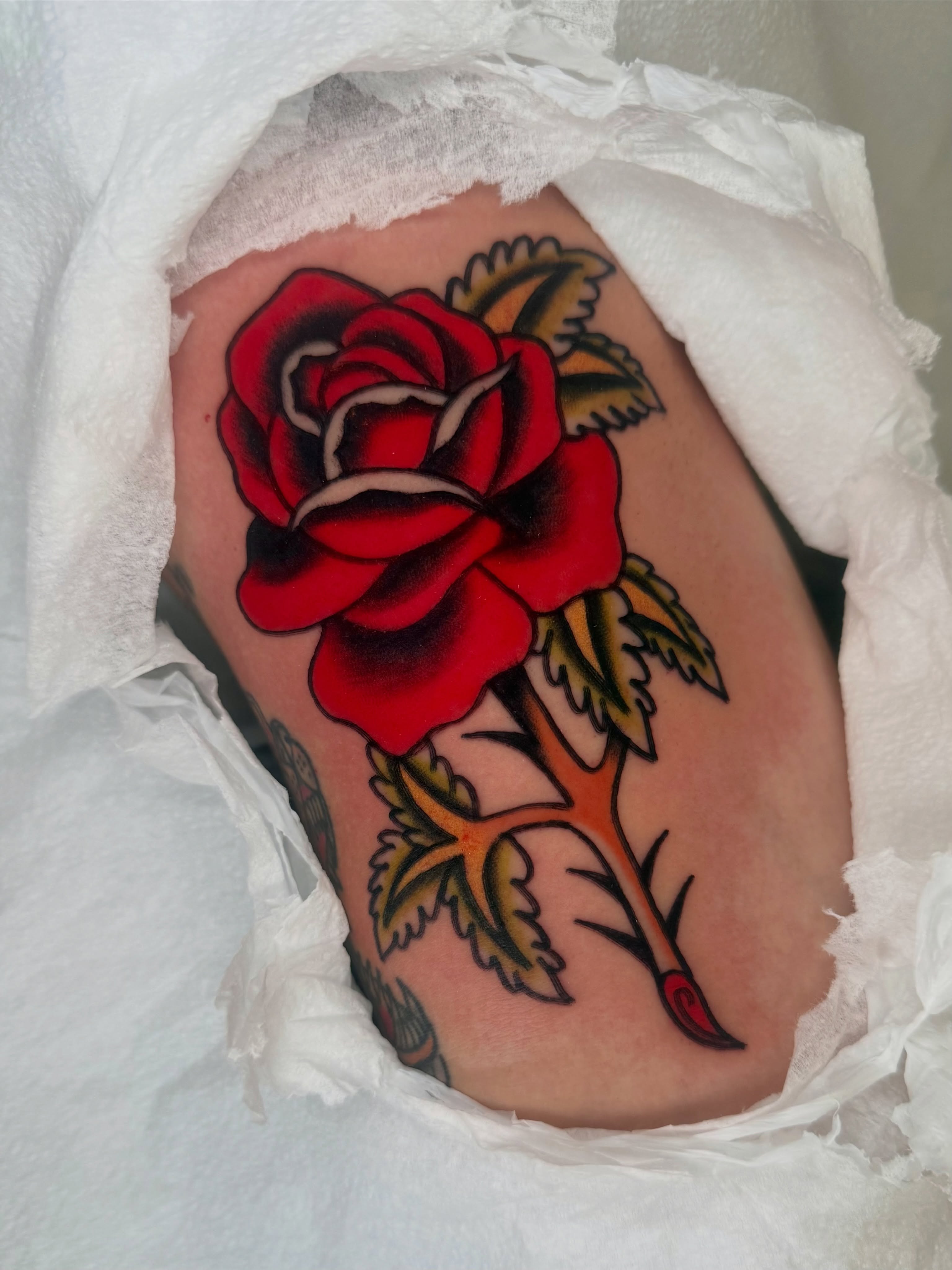 Red rose American traditional tattoo on the thigh by Lexie Graff