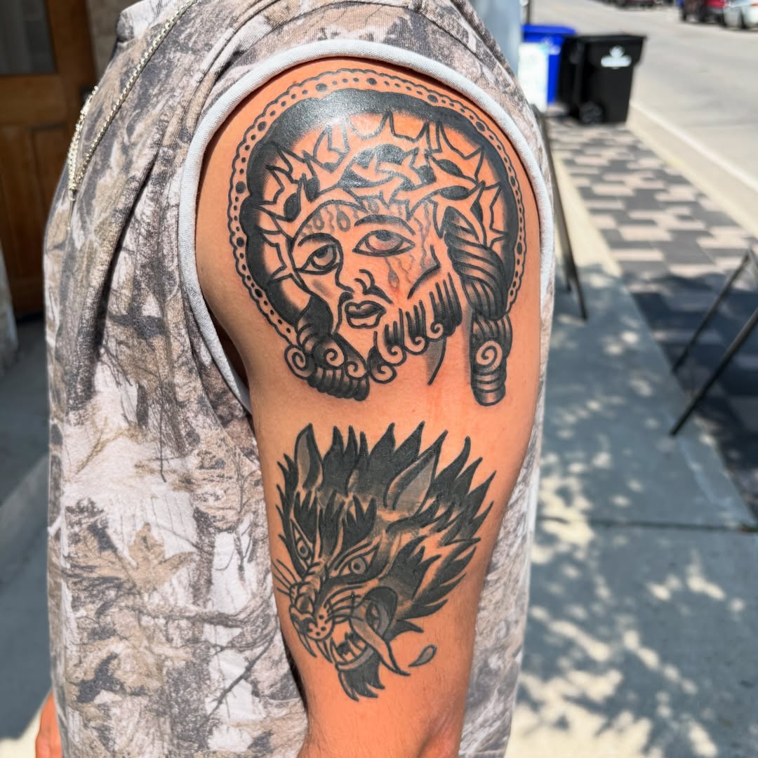 Bearded face with crown black and grey tattoo on the shoulder by Braedon 🎱