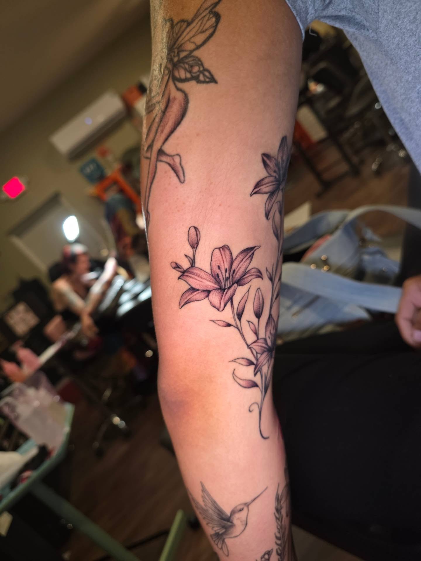Lilies and hummingbird new school tattoo on the forearm by Maggie