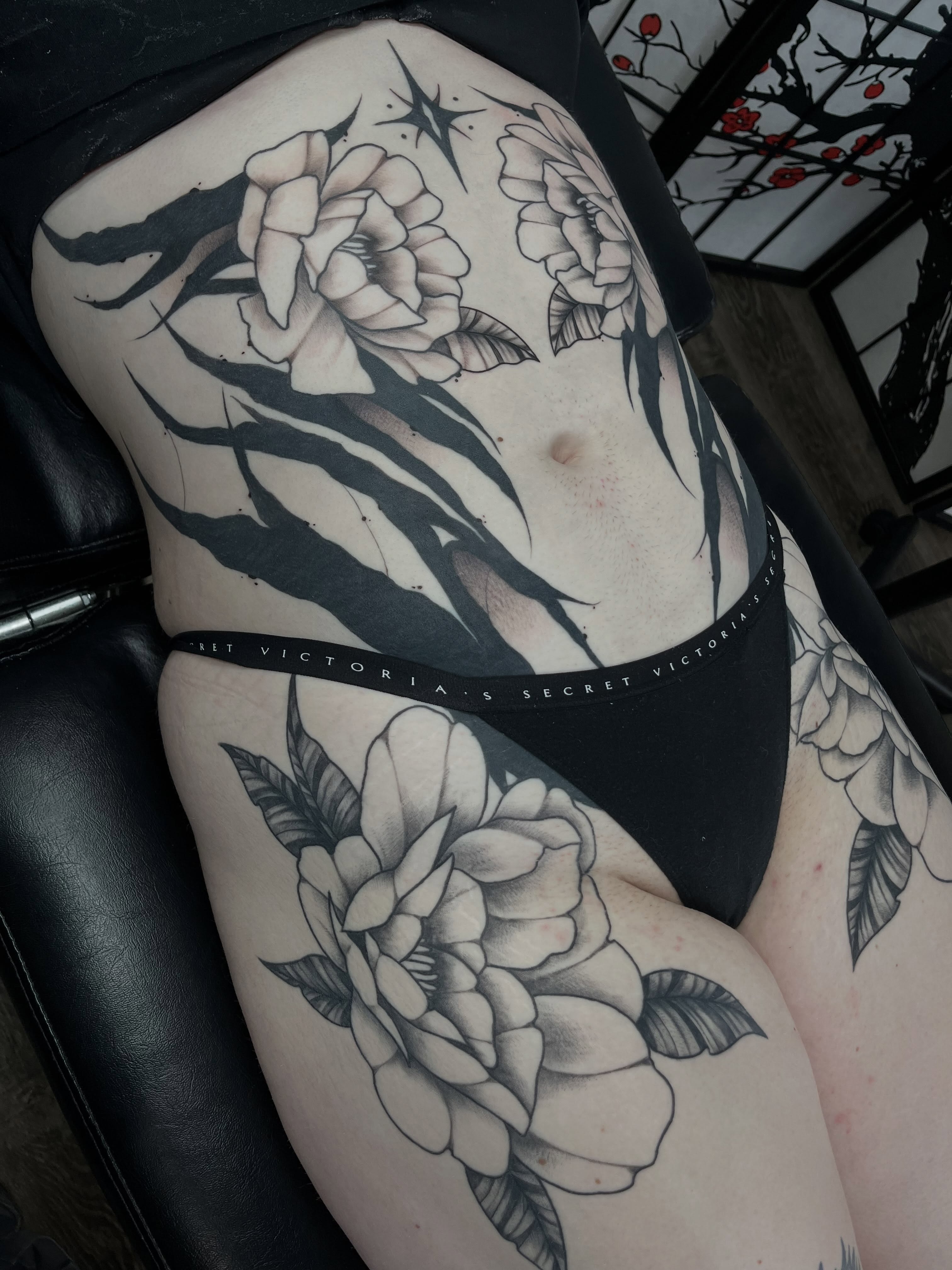 Floral black and grey tattoo on the thigh by Ty’s Tattoos