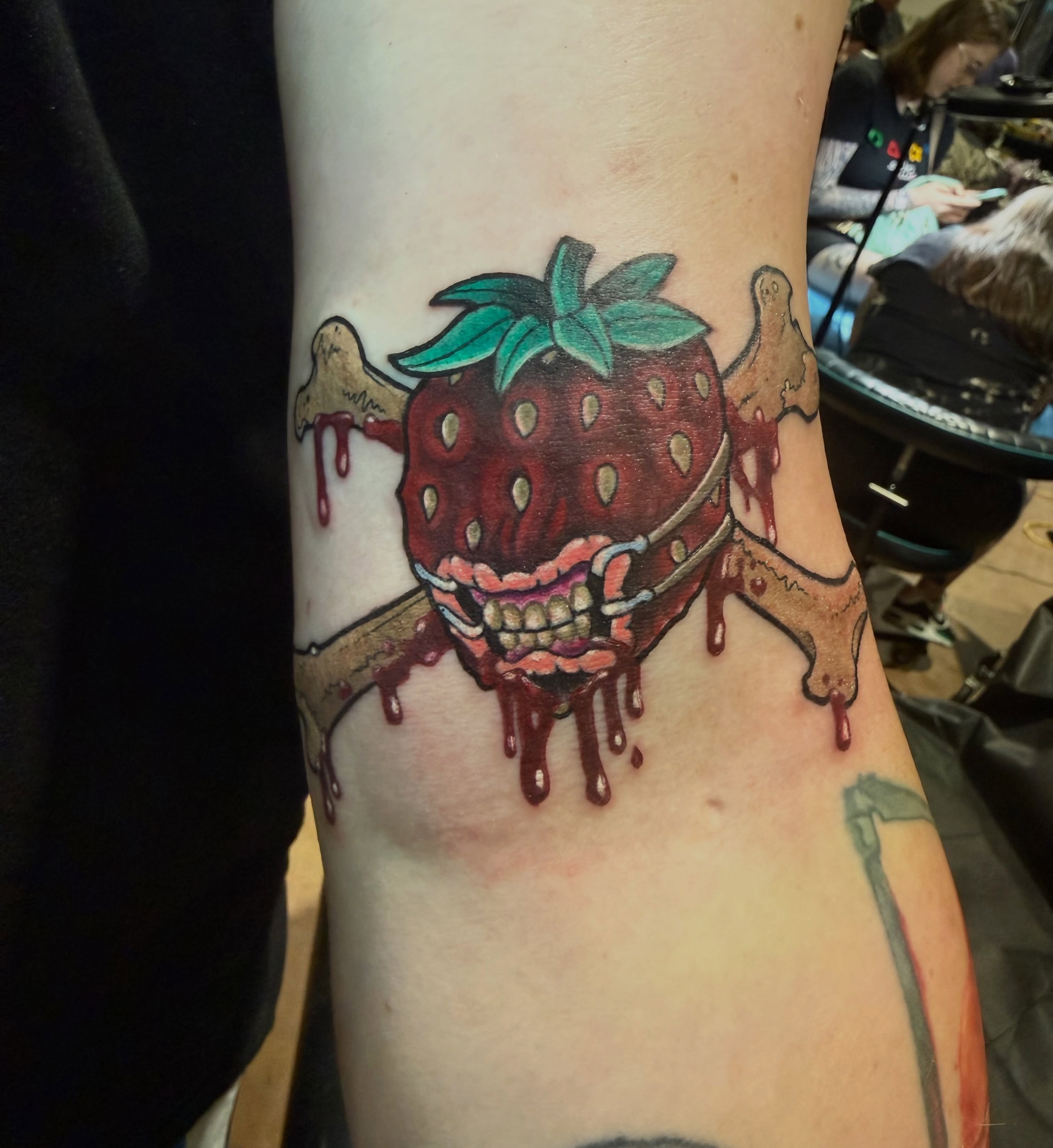 Strawberry with bones trash polka tattoo on the forearm by taylor mills