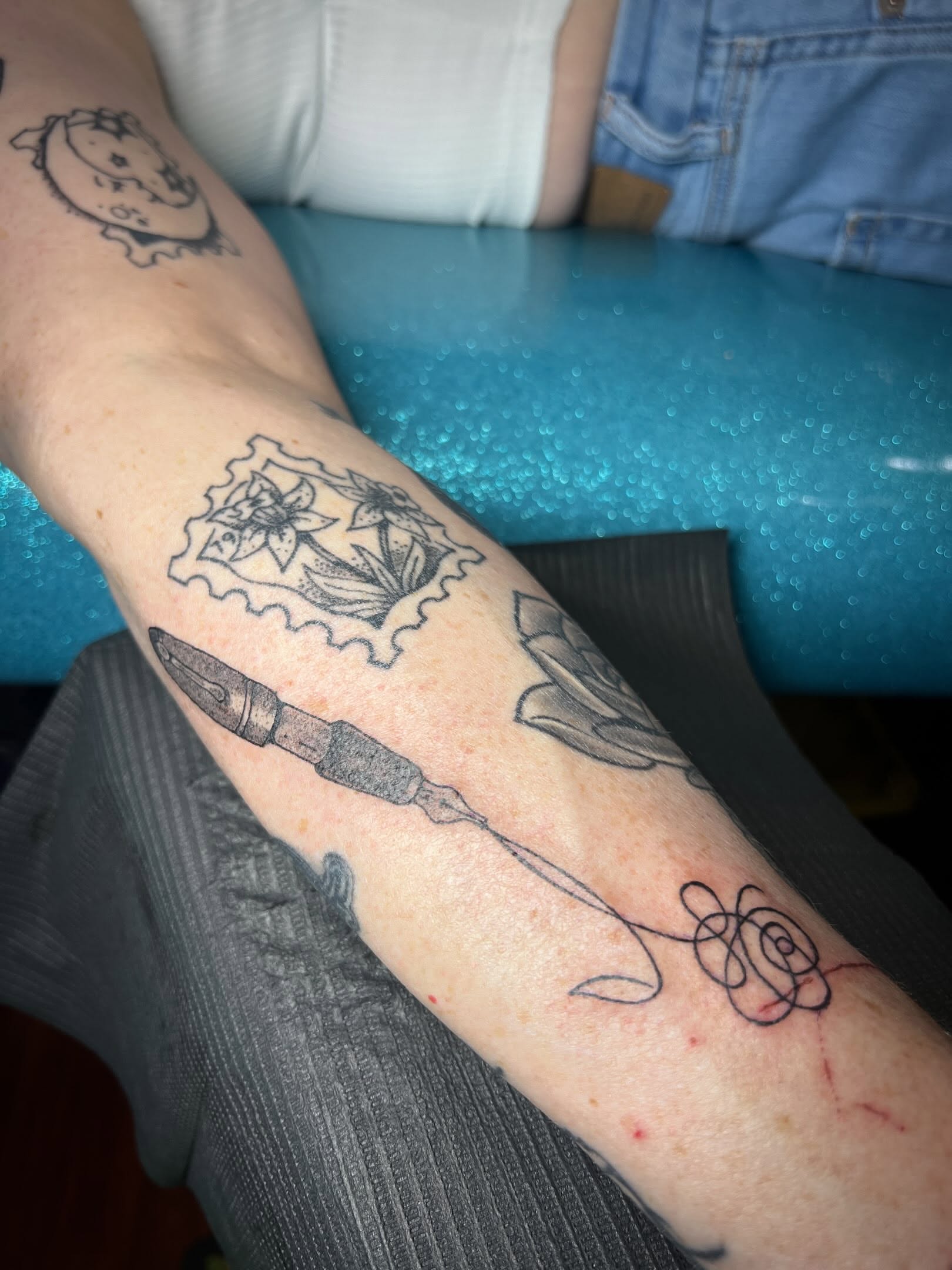 Pen and flower black and grey tattoo on the forearm by Tattoo Kayla