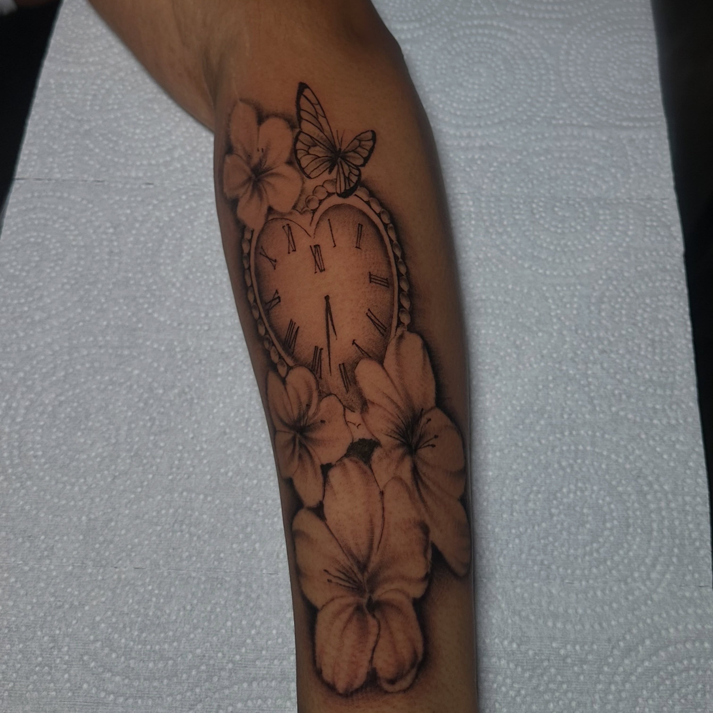 Clock with flowers black and grey tattoo on the forearm by @tattedbytuck