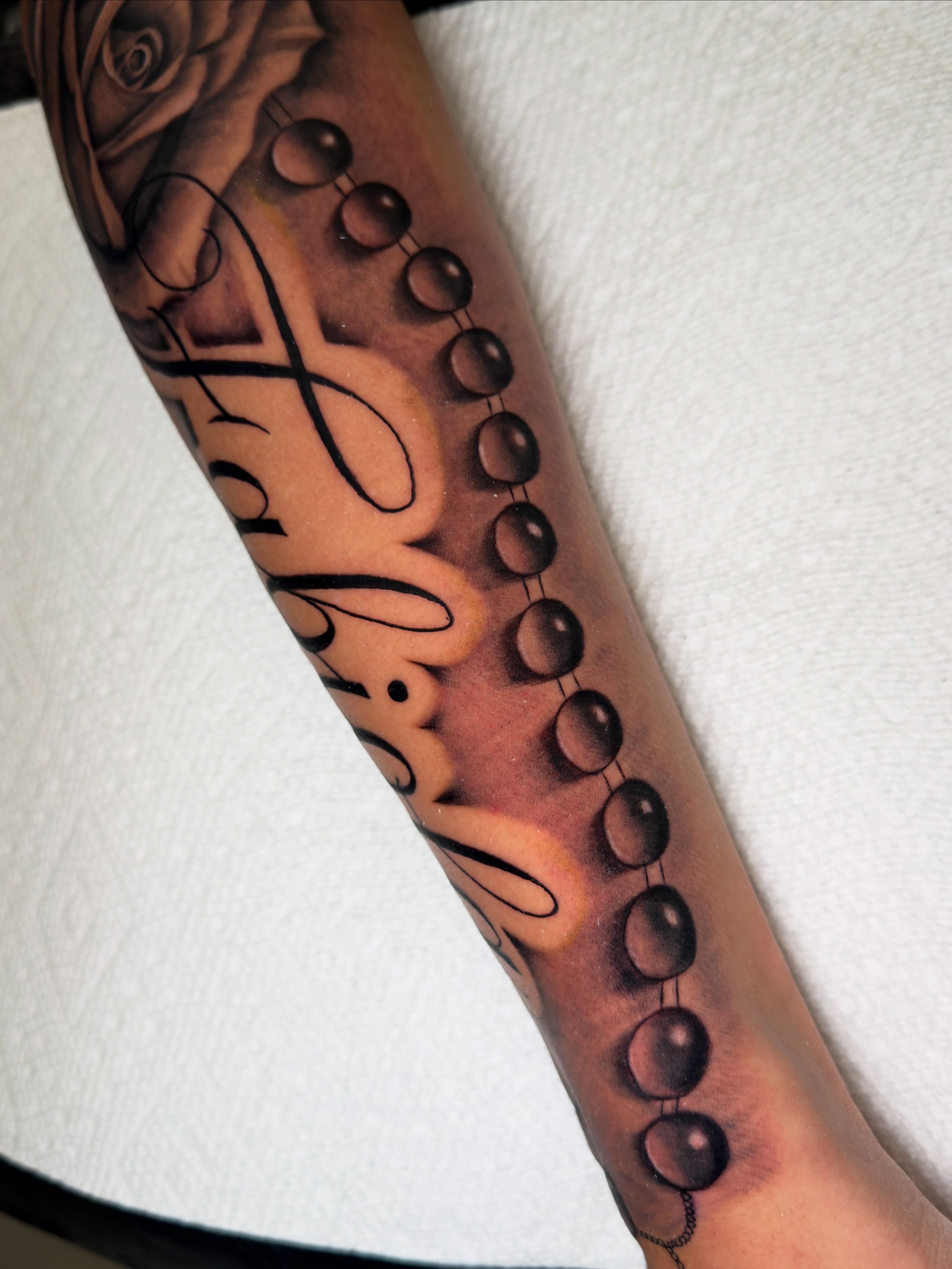 Beaded necklace black and grey tattoo on the forearm by Brandon Patino
