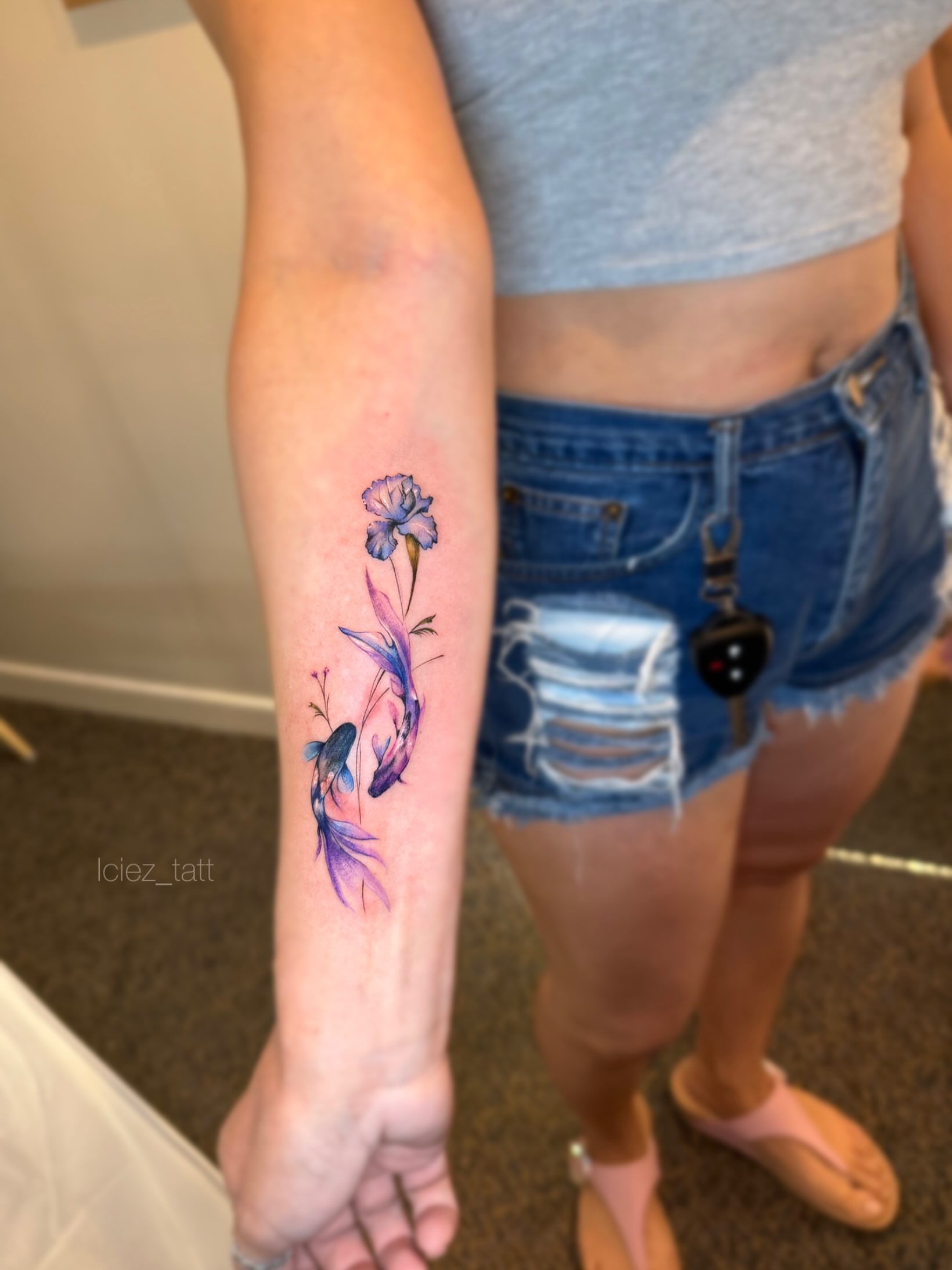 Fish and flowers watercolor tattoo on the forearm by Iciez