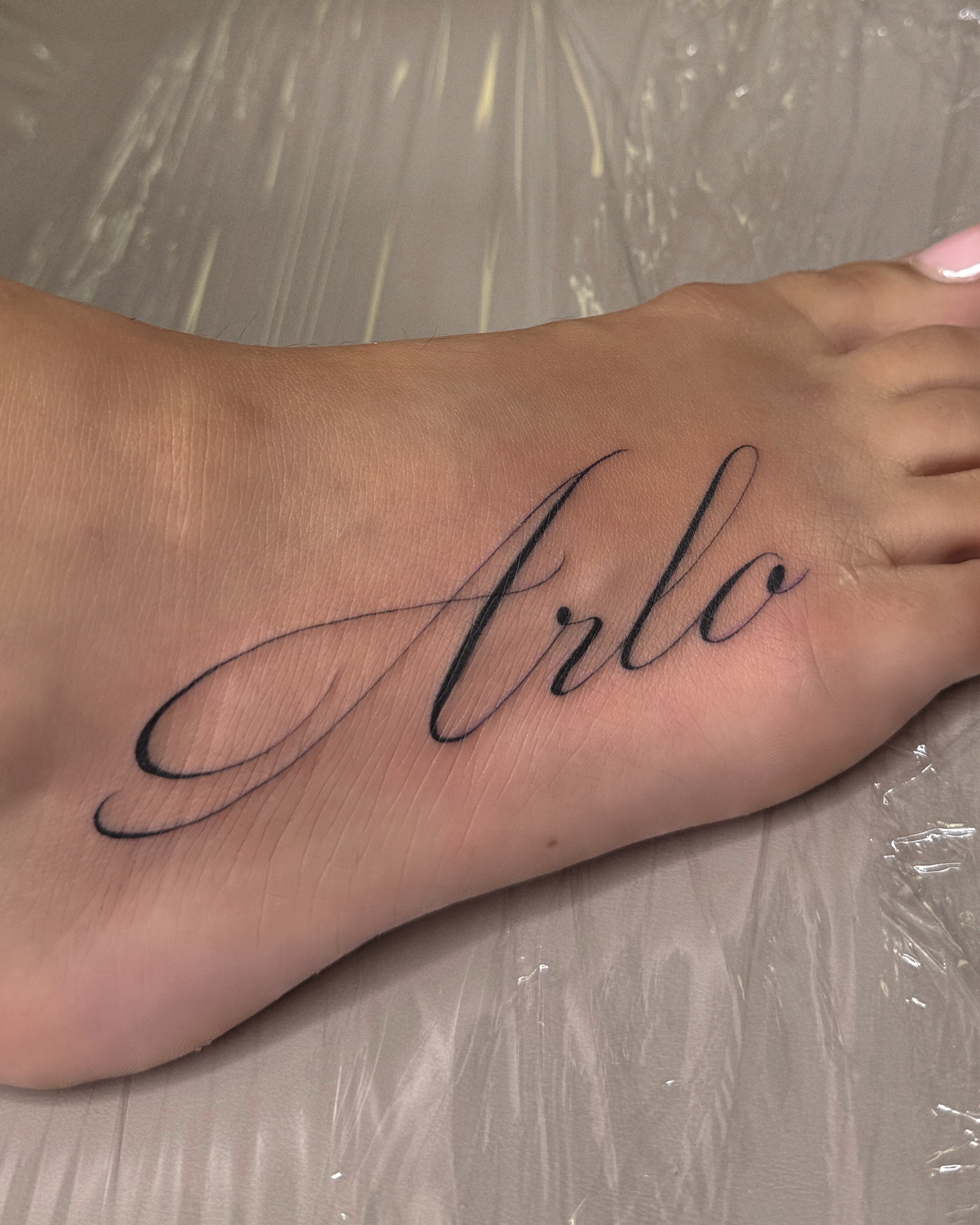 Arlo lettering script tattoo on the foot by Jennifer Garcia R - Vegas tattoo artist