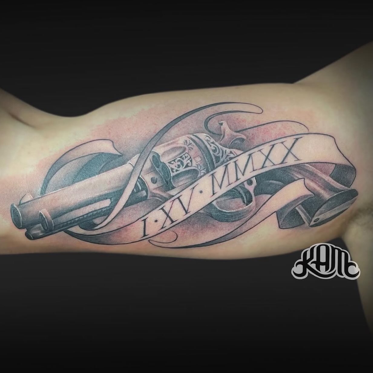 Gun and ribbon black and grey tattoo on the forearm by Keith (KAM) Miller