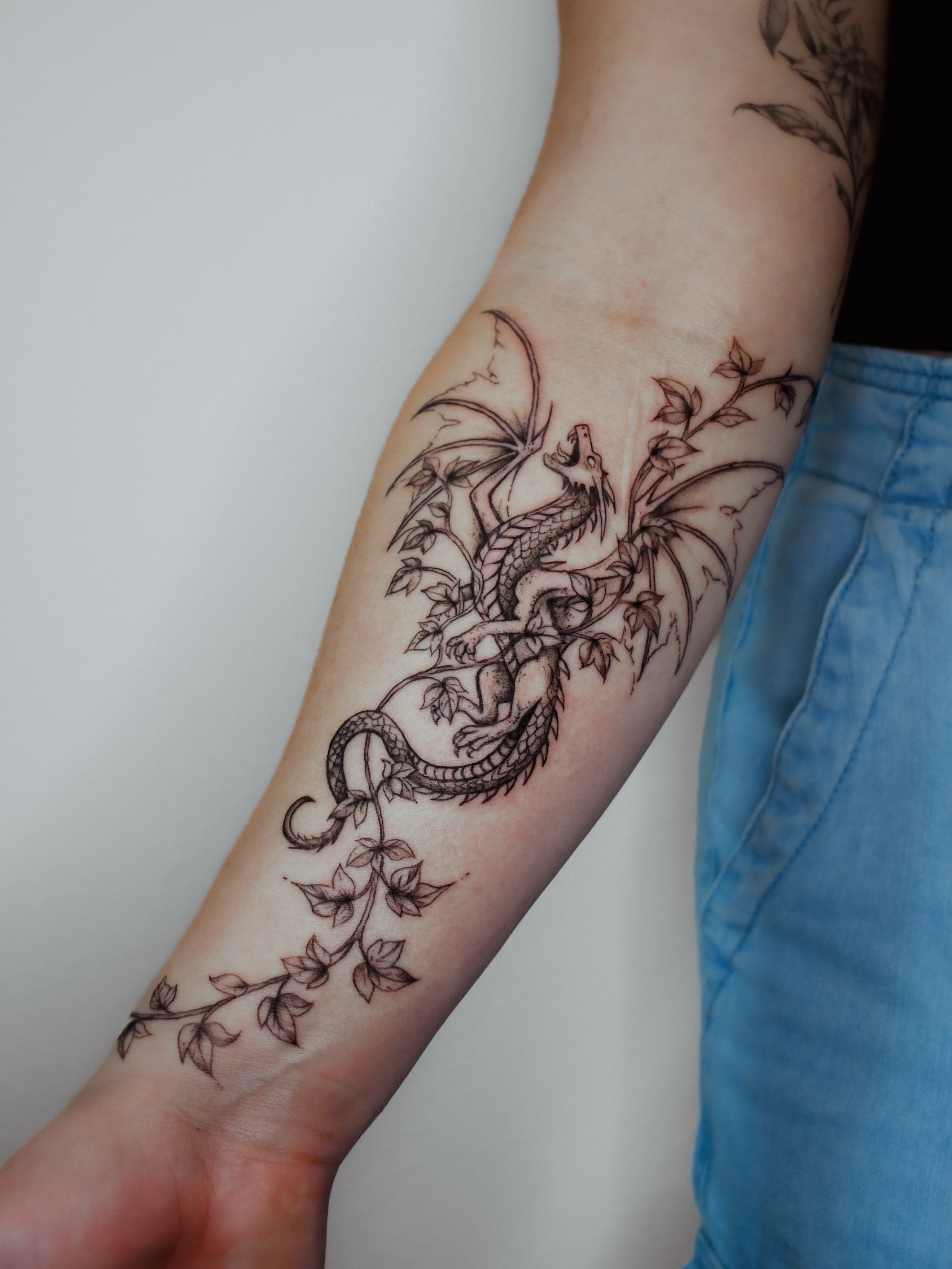 Dragon and leaves black and grey tattoo on the forearm by 𝐇𝐚𝐫𝐩𝐞𝐫
