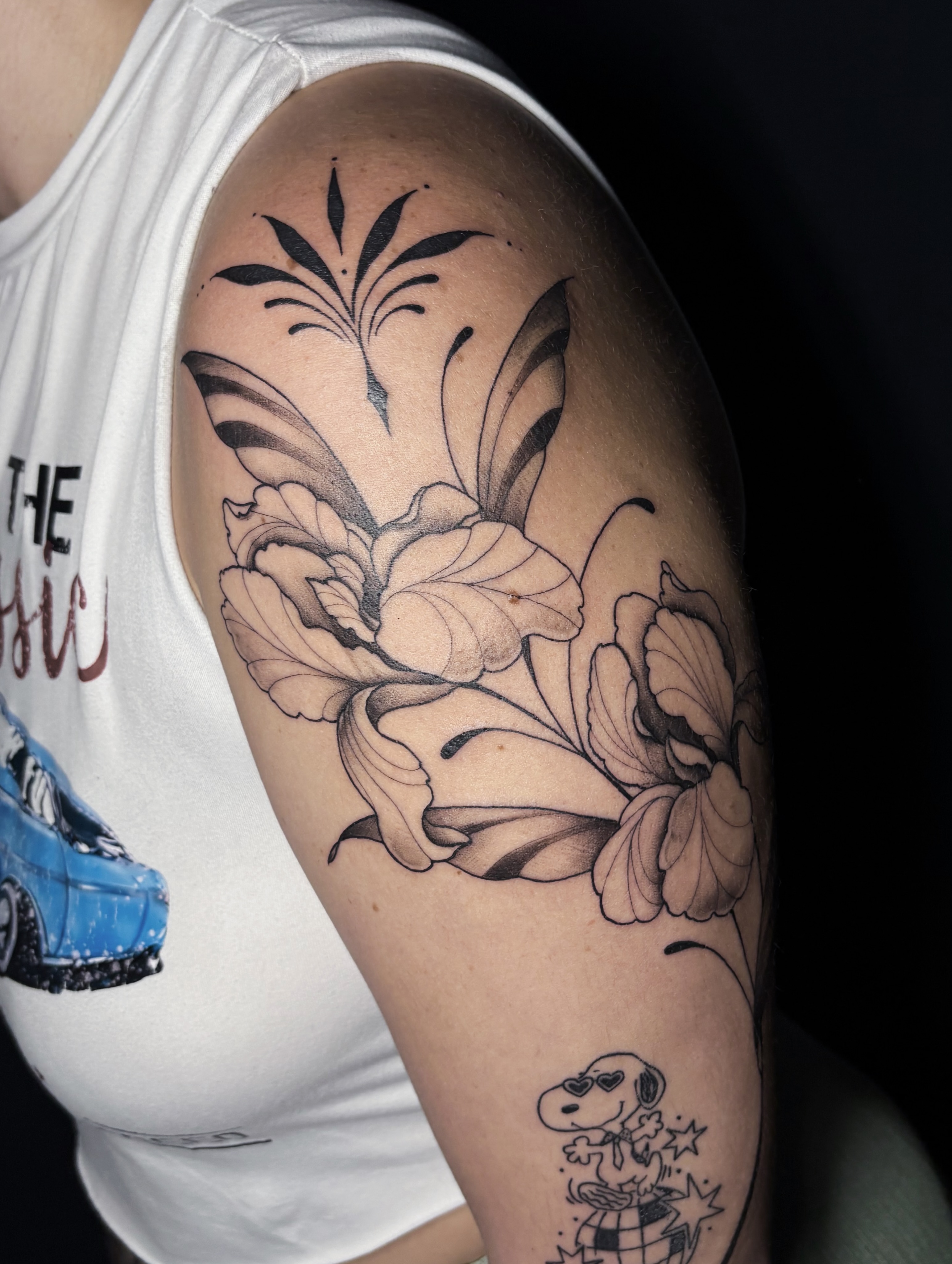 Floral arrangement black and grey tattoo on the upper arm by Fine Line Tattoo Artist