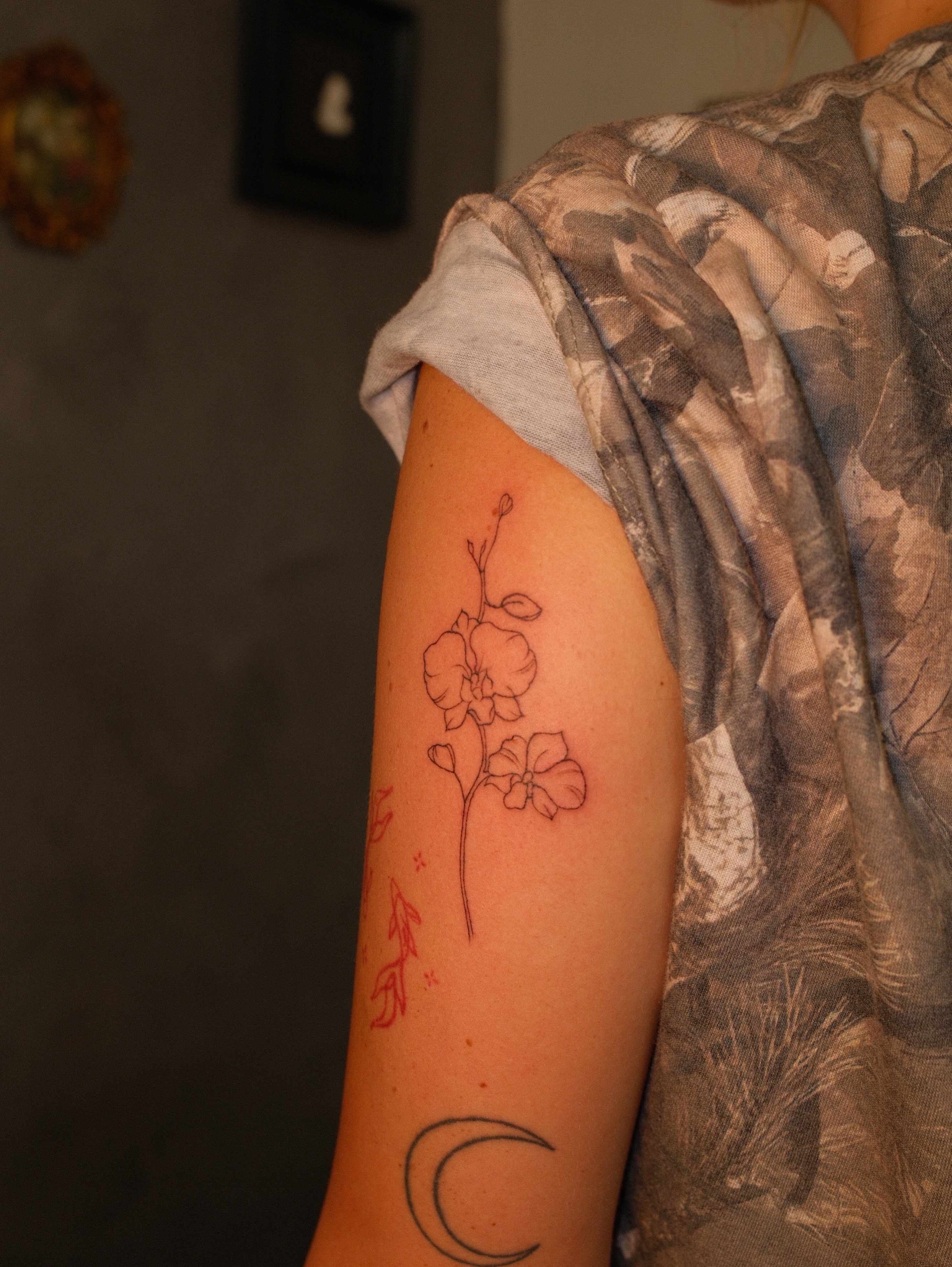 Flowers and crescent moon fine line tattoo on the upper arm by Luisa Duarte