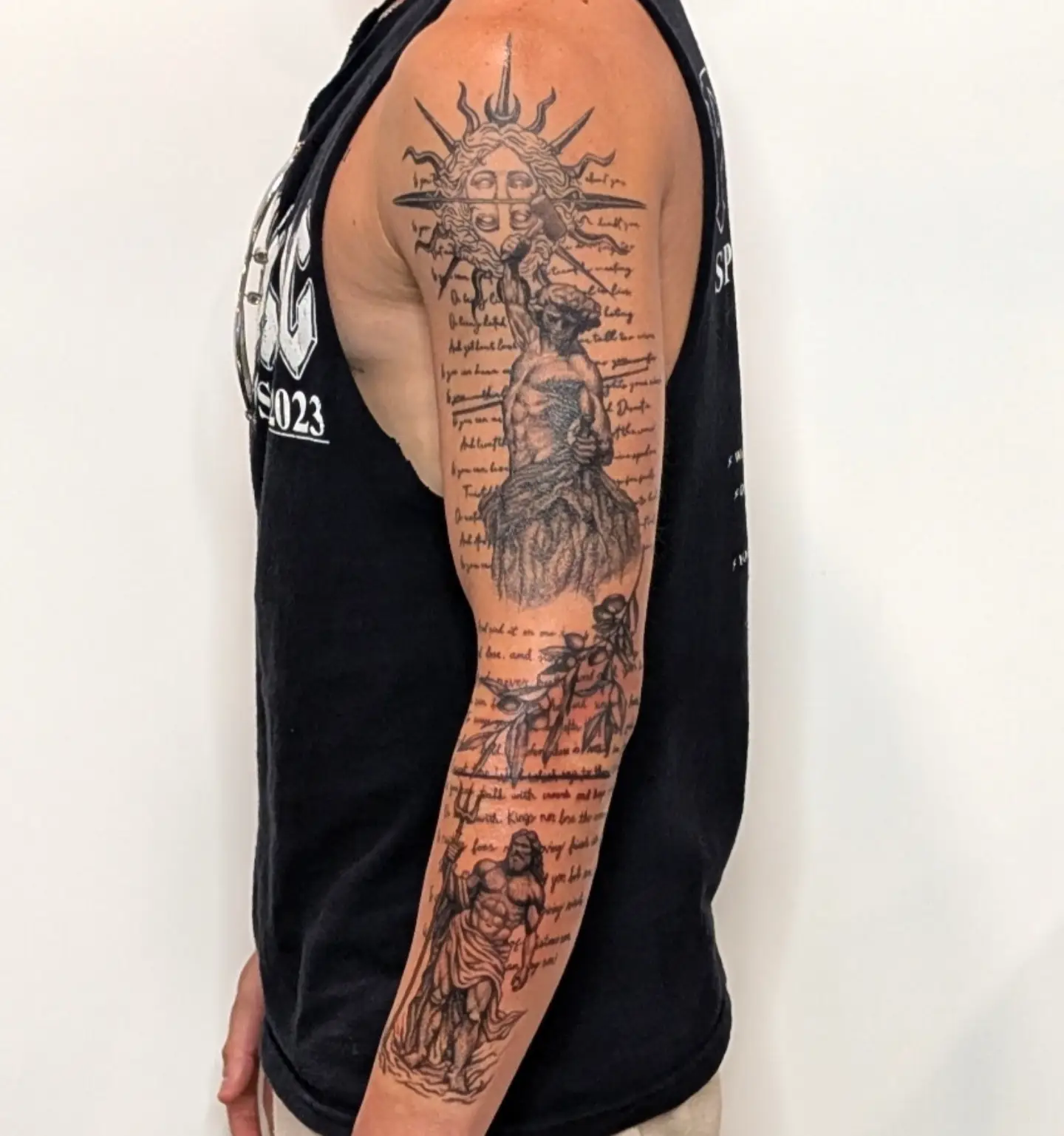 Statue and sun realism tattoo on the upper arm by Nenookaasi Martin