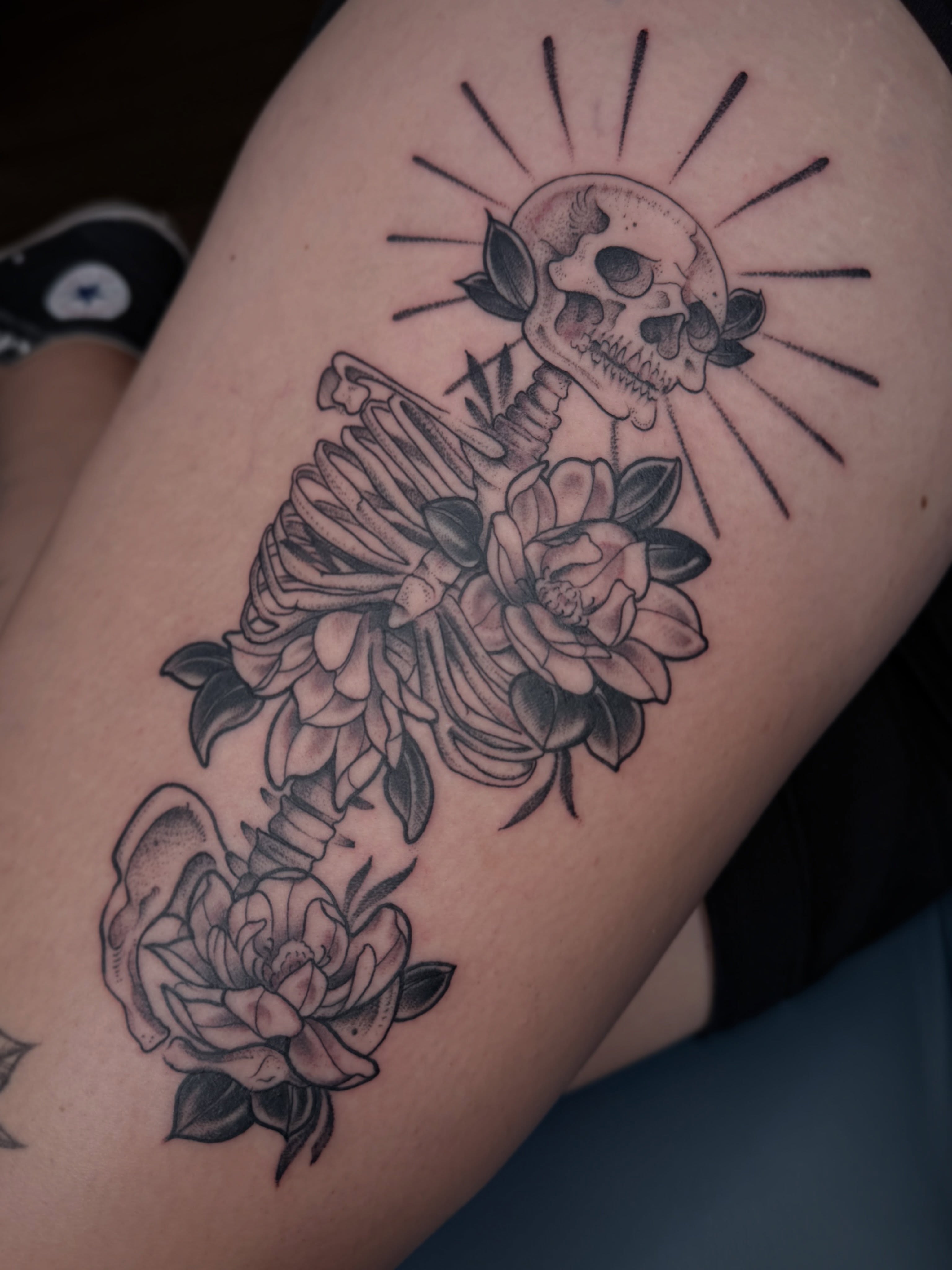 Skull and flowers black and grey tattoo on the thigh by Allyson Blessing Tattoos
