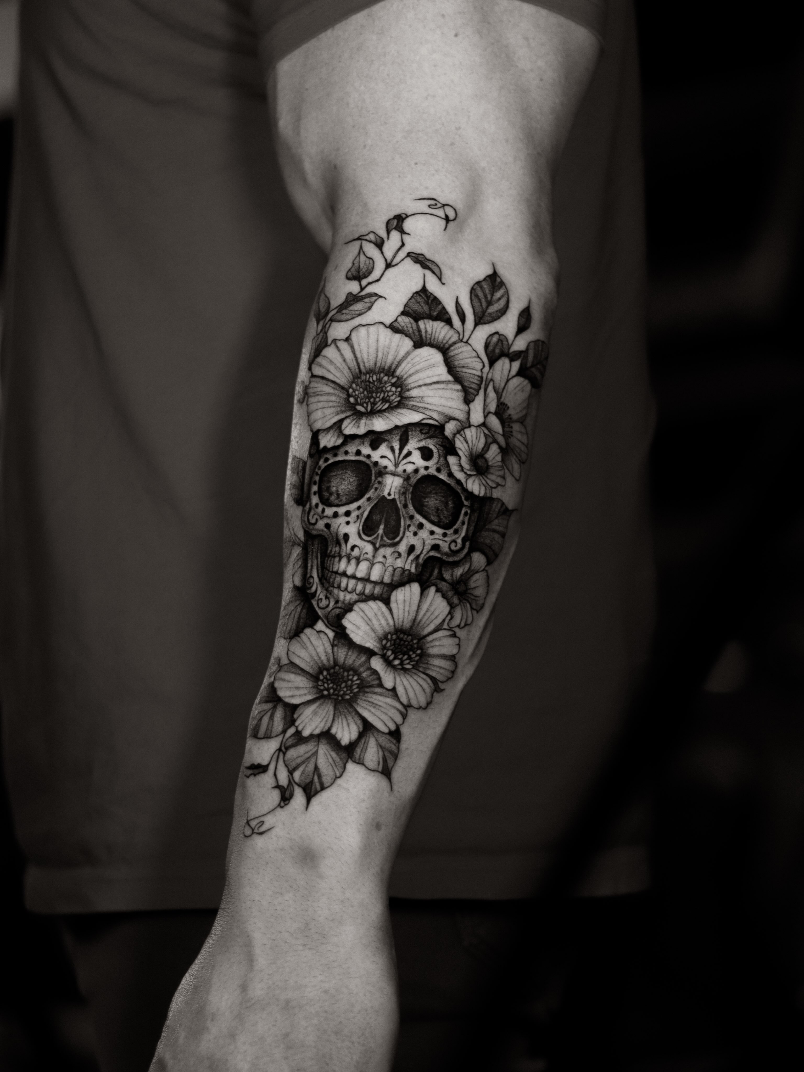 Skull and flowers black and grey tattoo on the forearm by Arthur Kossoski